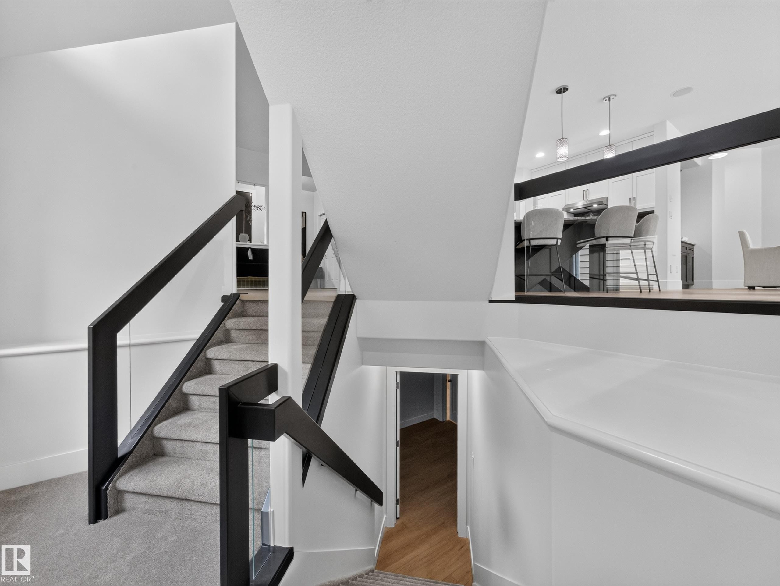 Staircase featuring black railings with glass panels and carpeted treads - #59 10550 Ellerslie Rd Sw, Edmonton, AB - Indoor Photo Showing Other Room