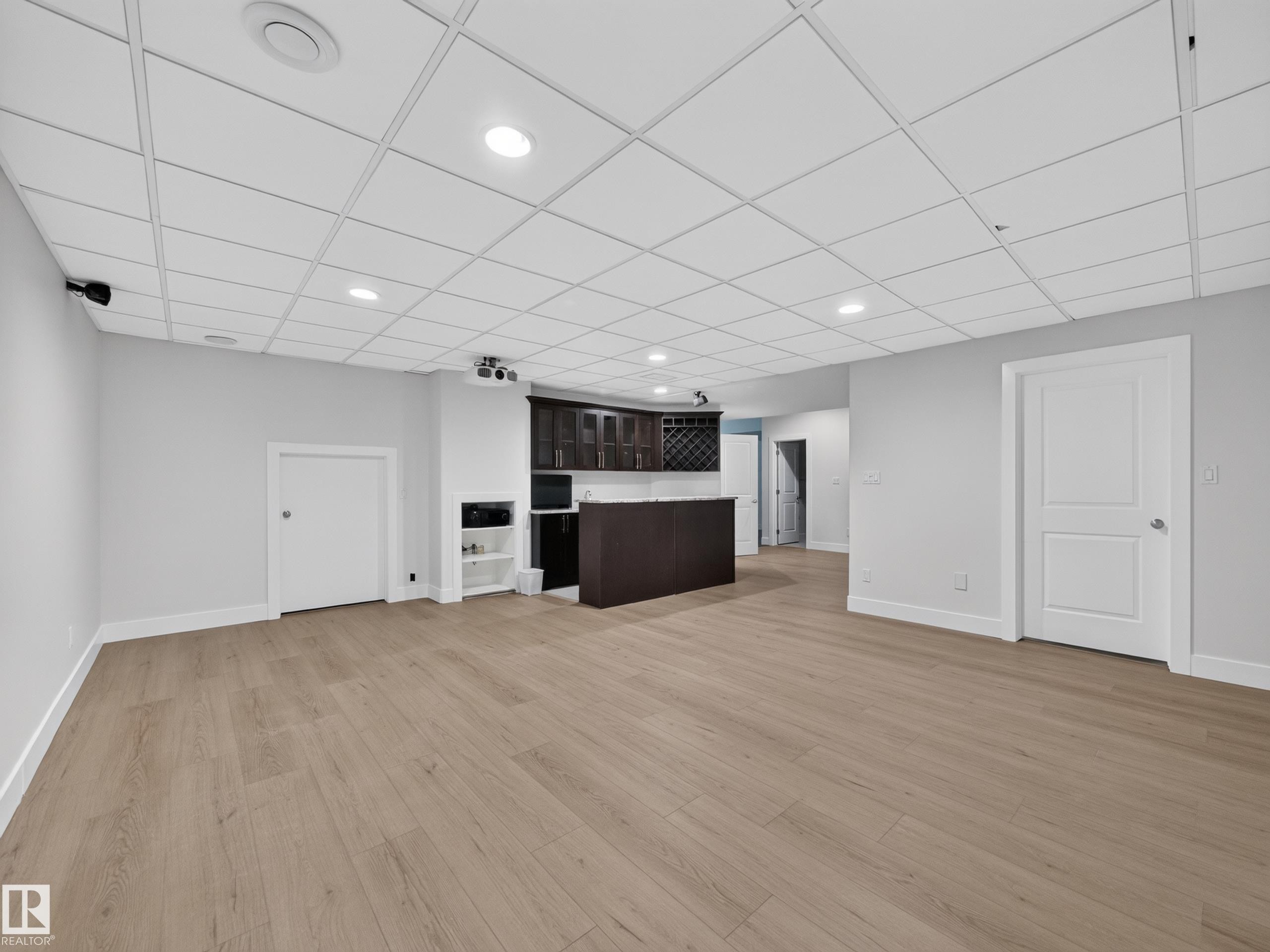 Spacious open room featuring wood-finish flooring, recessed lighting, and a built-in wet bar with dark cabinetry and a wine rack - #59 10550 Ellerslie Rd Sw, Edmonton, AB - Indoor