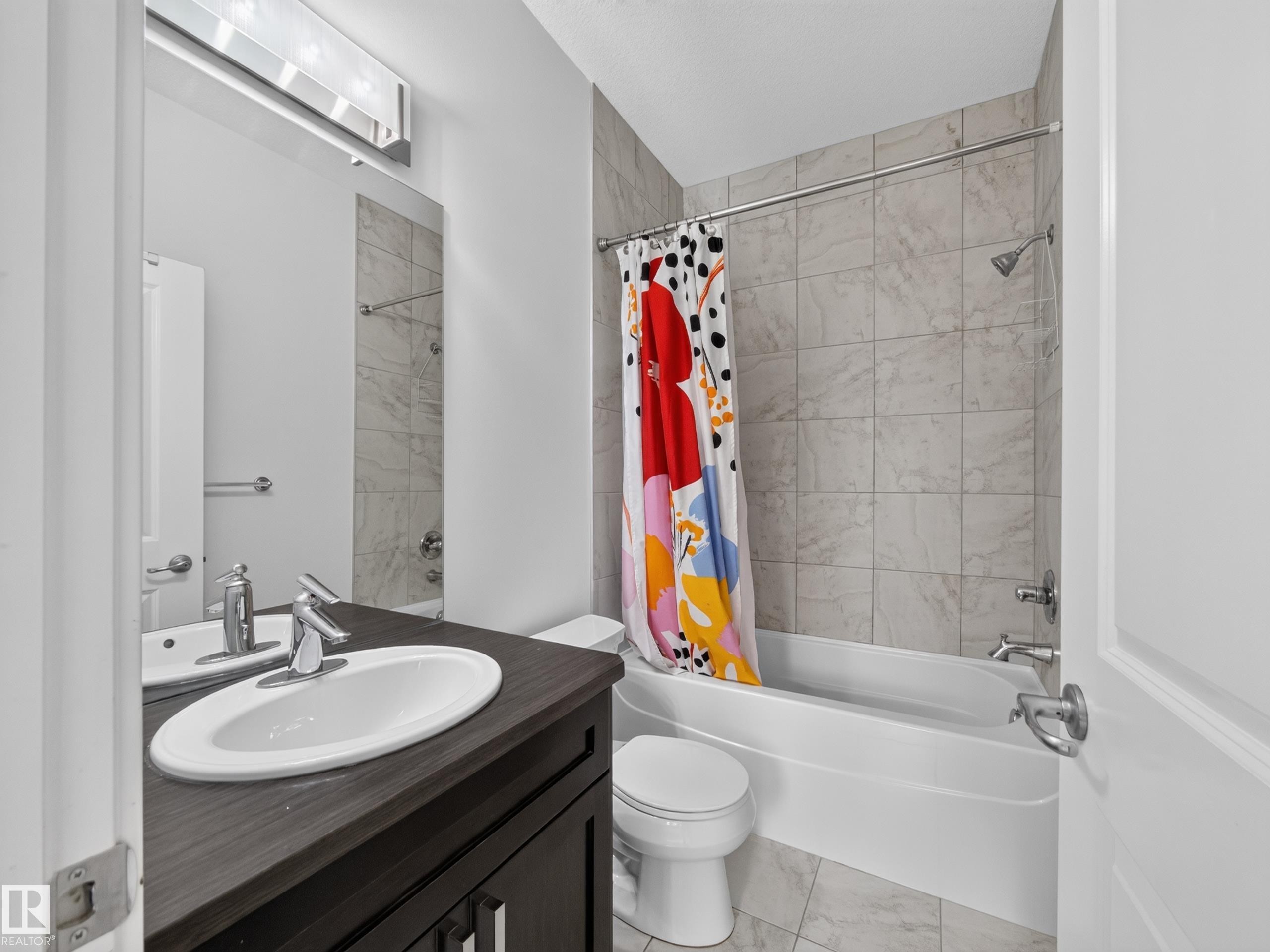 Bathroom featuring a dark wood-finish vanity, white undermount sink, chrome faucet, and expansive mirror - #59 10550 Ellerslie Rd Sw, Edmonton, AB - Indoor Photo Showing Bathroom