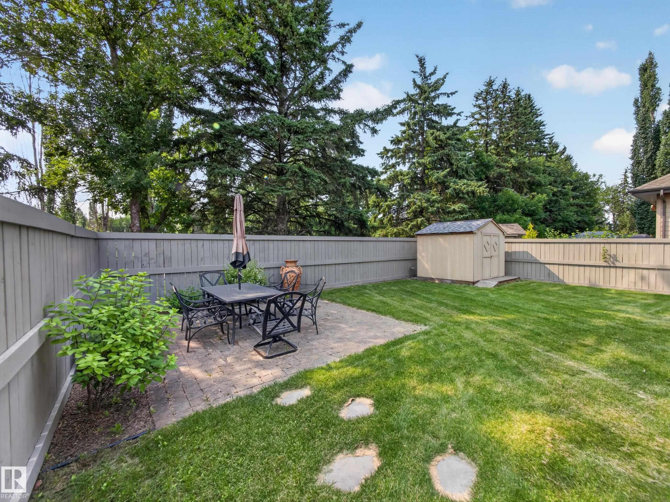 Spacious backyard featuring a paver patio area, green lawn, and a storage shed - #59 10550 Ellerslie Rd Sw, Edmonton, AB - Outdoor With Backyard