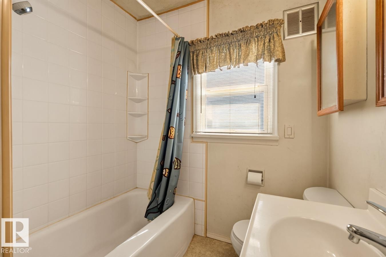 White tiled tub/shower combination with integrated corner shelving, single hung window with blinds, wall-mounted medicine cabinet with wood trim, and a white vanity with an integrated sink - 12309 128 Street Nw, Edmonton, AB