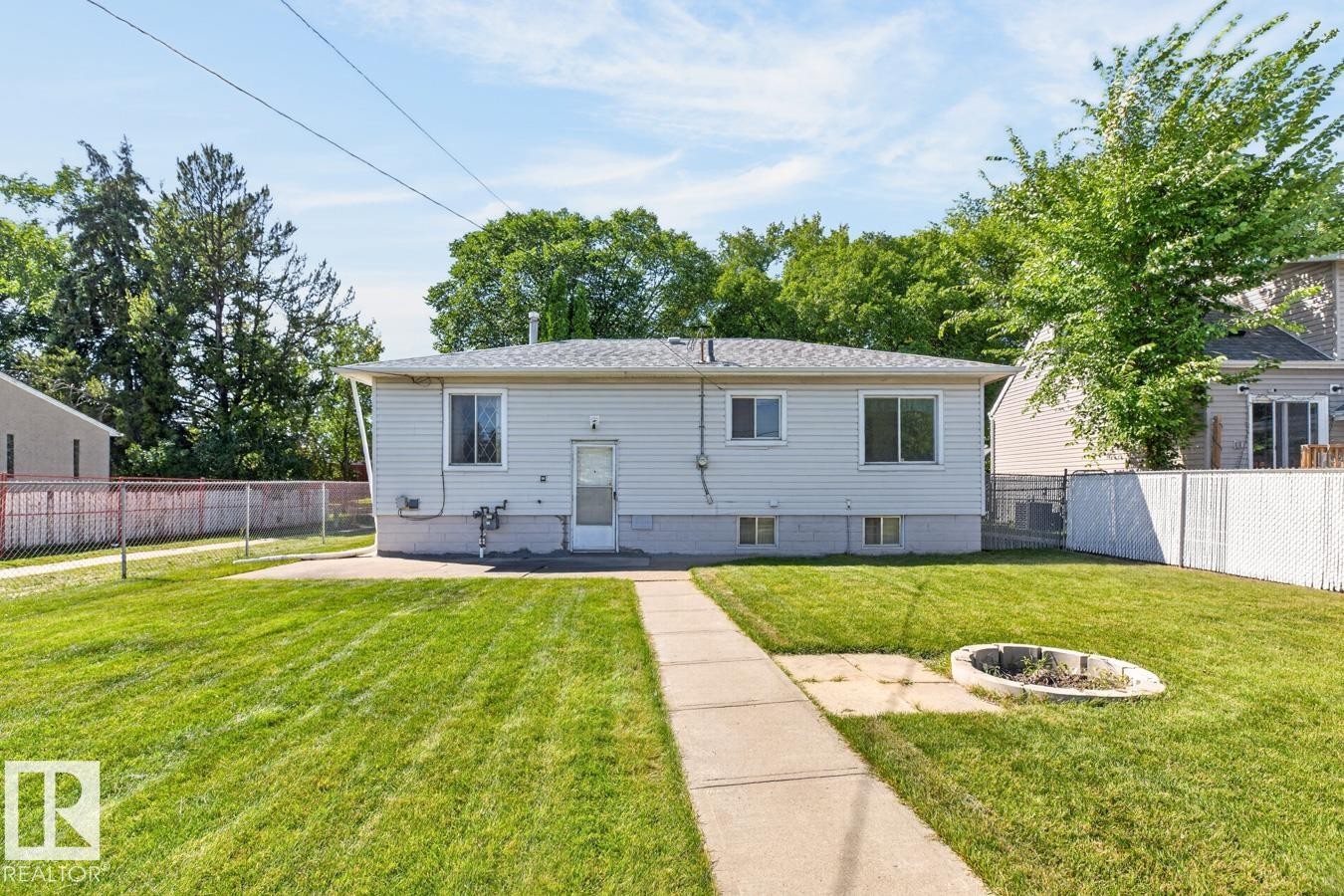 Expansive lawn featuring a concrete pathway, a built-in fire pit, and a chain-link fence - 12309 128 Street Nw, Edmonton, AB