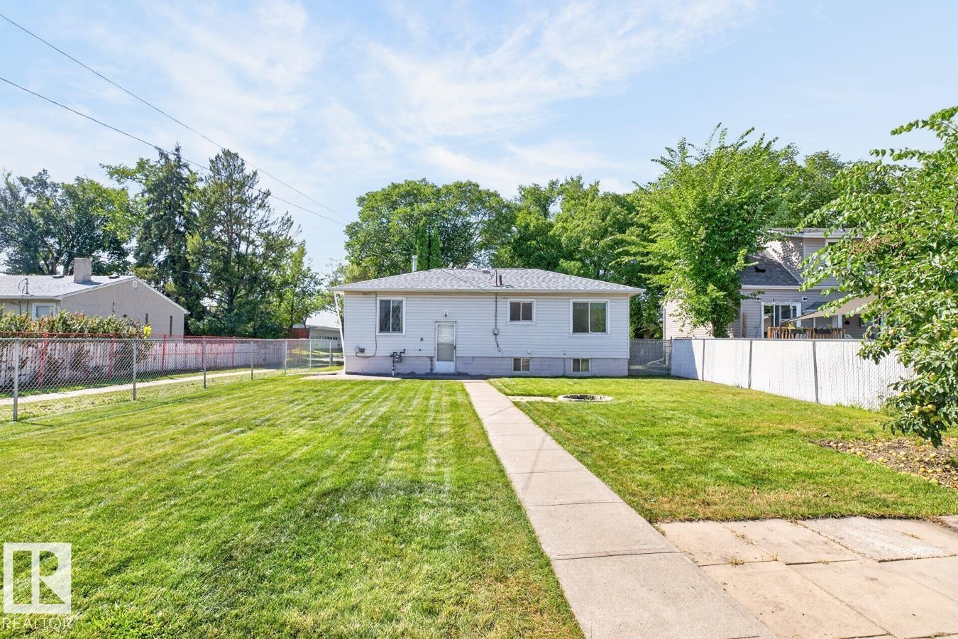 Expansive backyard featuring a manicured lawn, concrete pathway, and mature trees, enclosed by a chain link fence and a privacy fence - 12309 128 Street Nw, Edmonton, AB