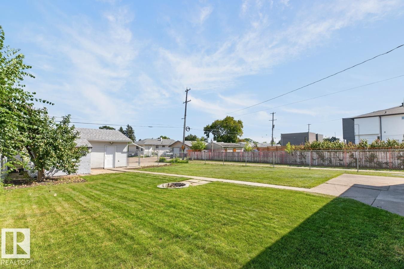 Expansive green lawn with a built-in fire pit, concrete pathways, and a detached garage with a shingled roof - 12309 128 Street Nw, Edmonton, AB