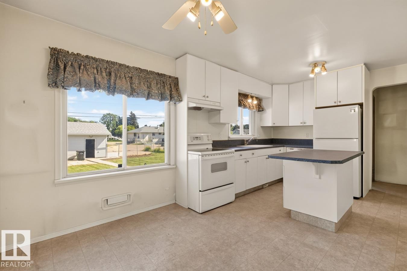 Kitchen featuring white cabinetry, a built-in island, white appliances, and a window overlooking the property - 12309 128 Street Nw, Edmonton, AB