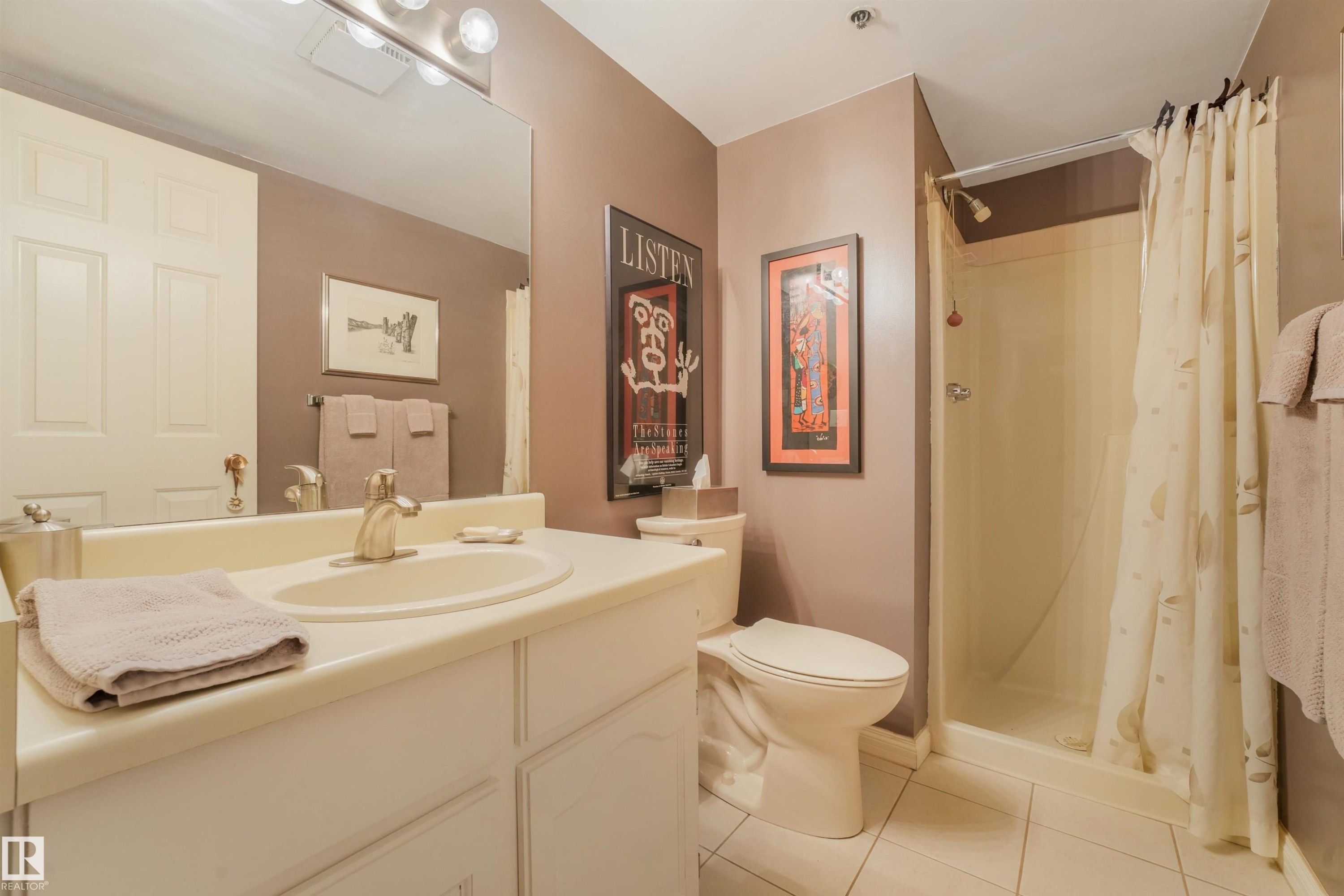 Single vanity with an integrated sink and brushed nickel faucet, a toilet, and a stand-up shower with a shower curtain - #203 10171 119 St Nw, Edmonton, AB