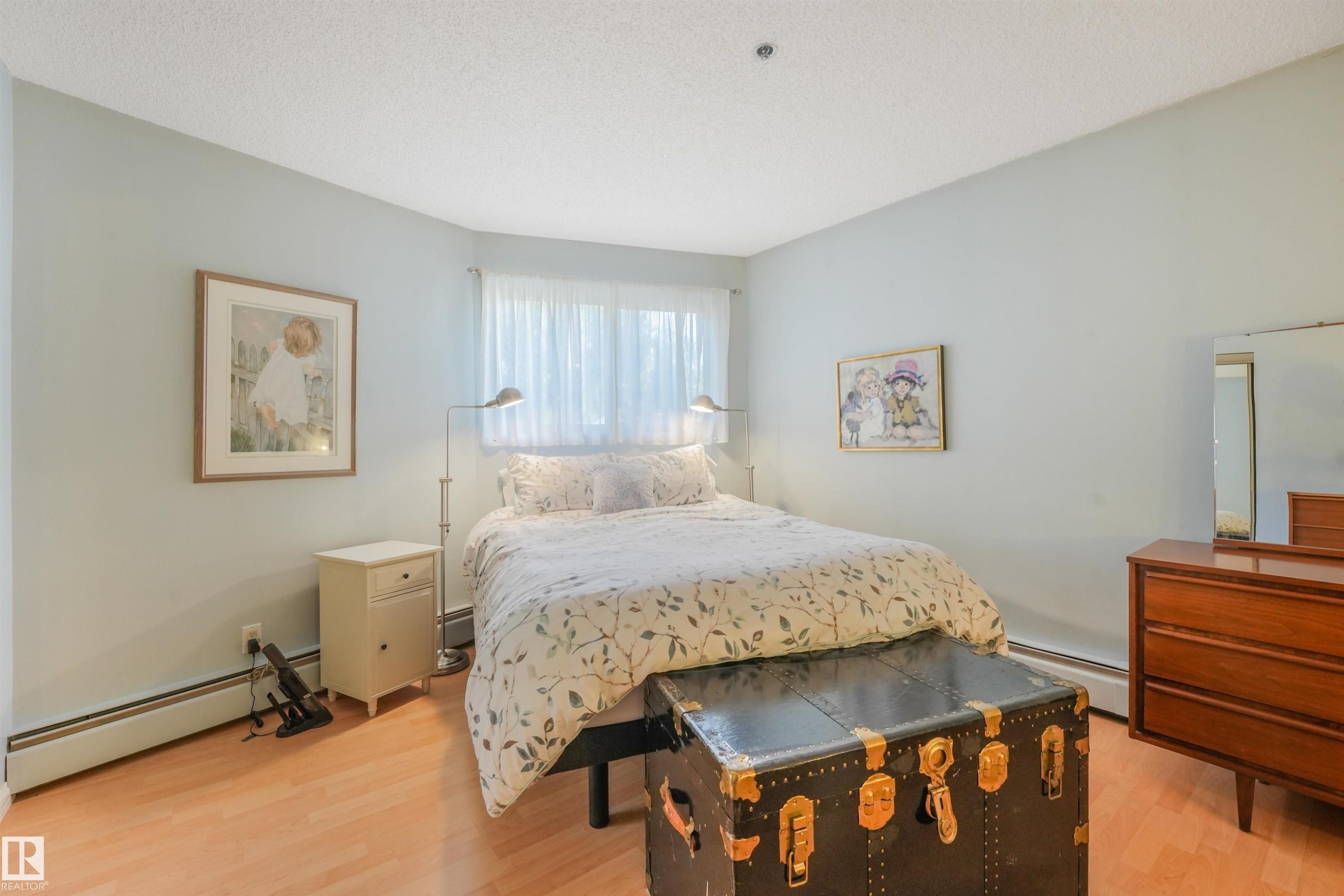 Wood-finish flooring, light-toned walls, and a window with sheer curtains - #203 10171 119 St Nw, Edmonton, AB
