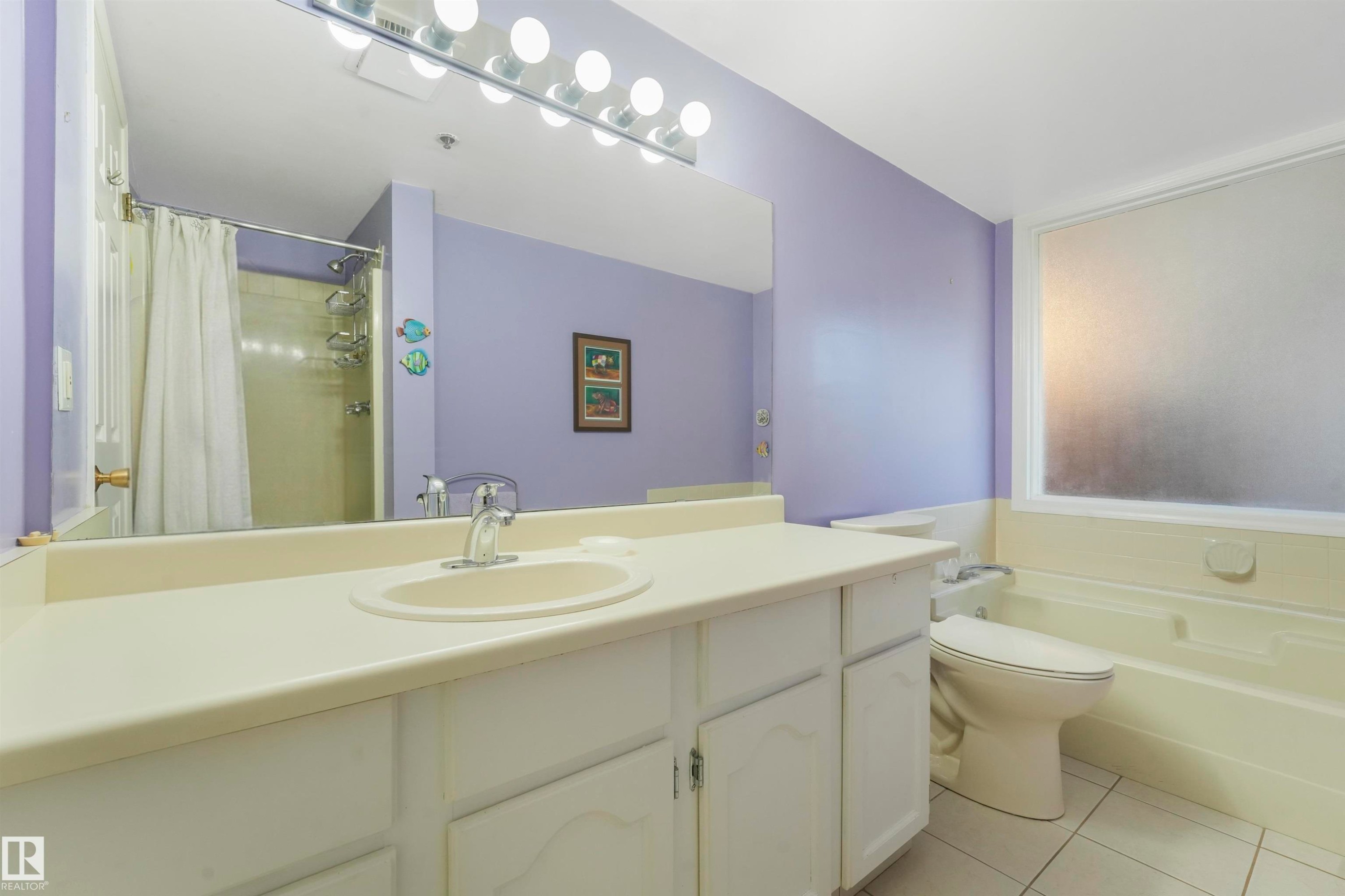 Spacious vanity with an integrated sink and chrome faucet, tile flooring, and a frosted window above the tub - #203 10171 119 St Nw, Edmonton, AB