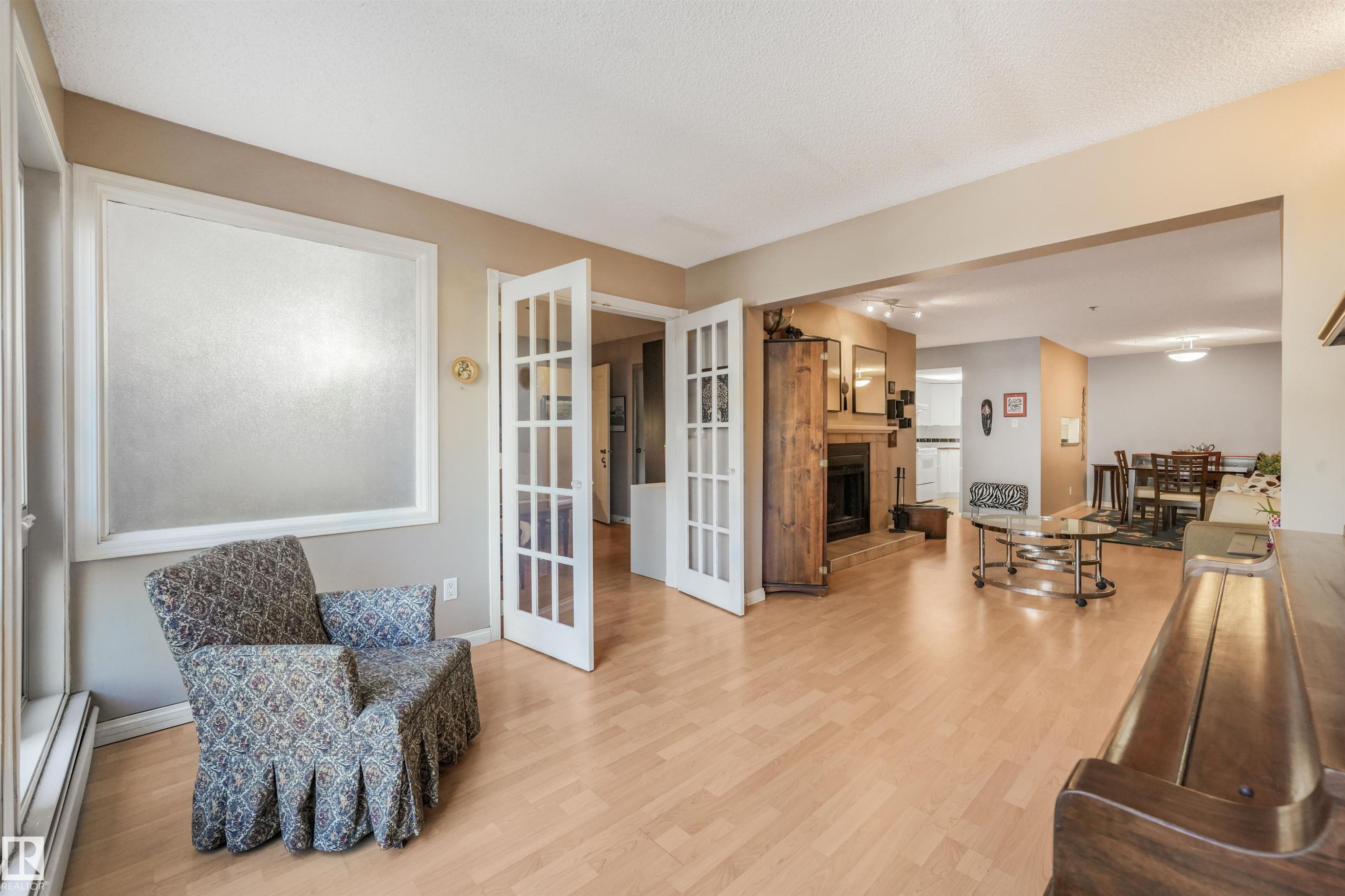 Wood-finish flooring throughout, French doors, recessed lighting, and a built-in fireplace with a stone surround - #203 10171 119 St Nw, Edmonton, AB