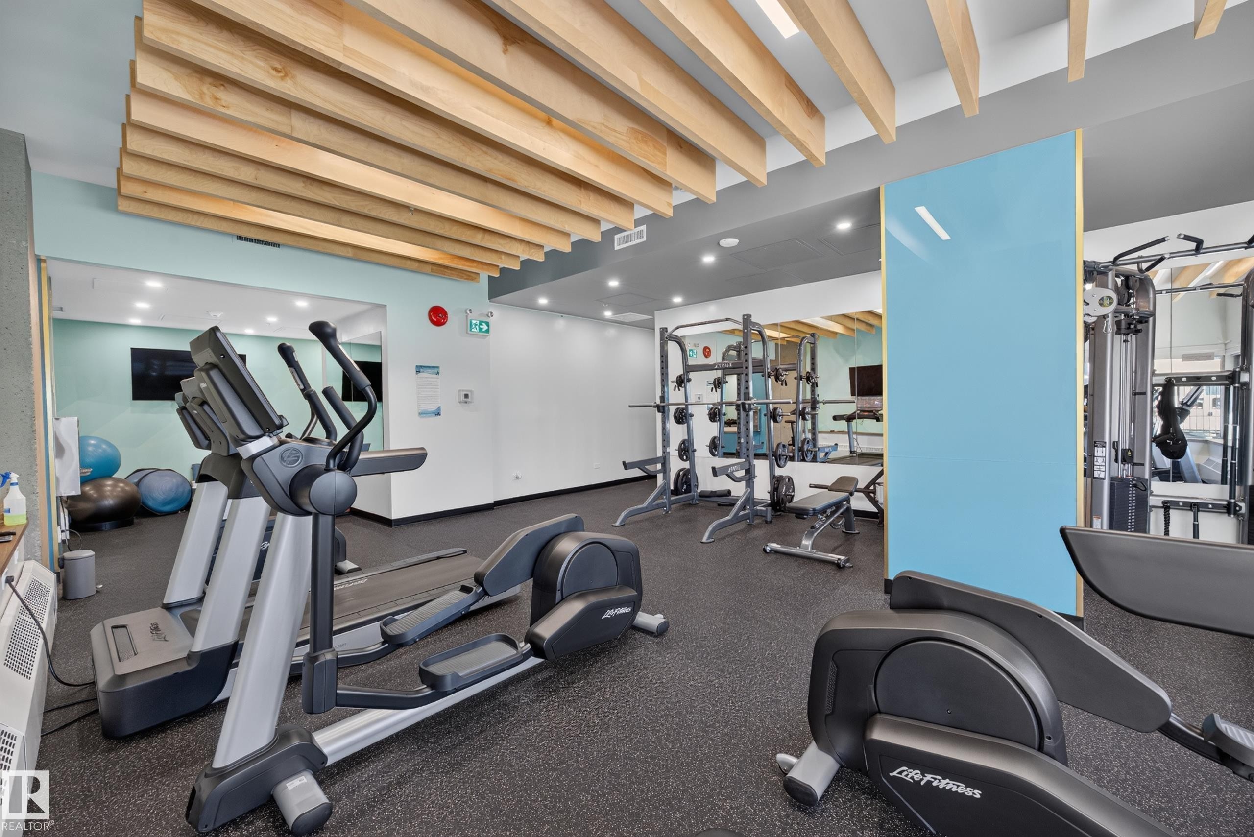 Condo Building Gym Space featuring rubber flooring, ample equipment, and a view of the common area grounds. - #803 10011 123 St Nw, Edmonton, AB