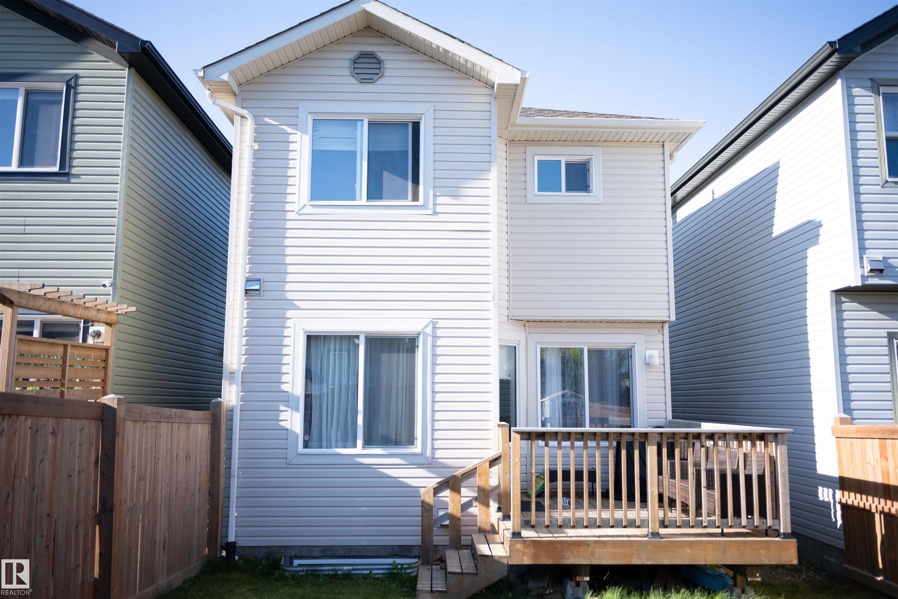 Two-story exterior with light-colored siding, multiple windows, and a wooden deck with railings - 9014 Cooper Link Link Sw, Edmonton, AB
