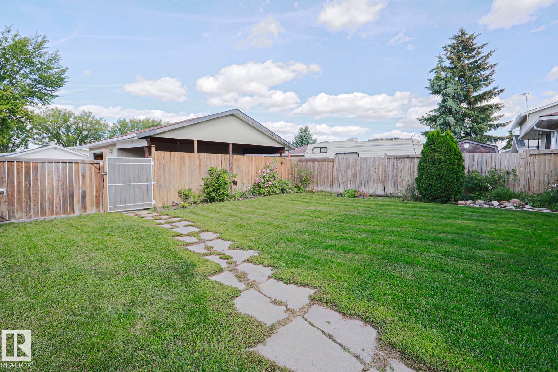 Expansive lawn with a stone pathway, wood fencing, and mature perimeter trees - 11440 144 Avenue Nw, Edmonton, AB