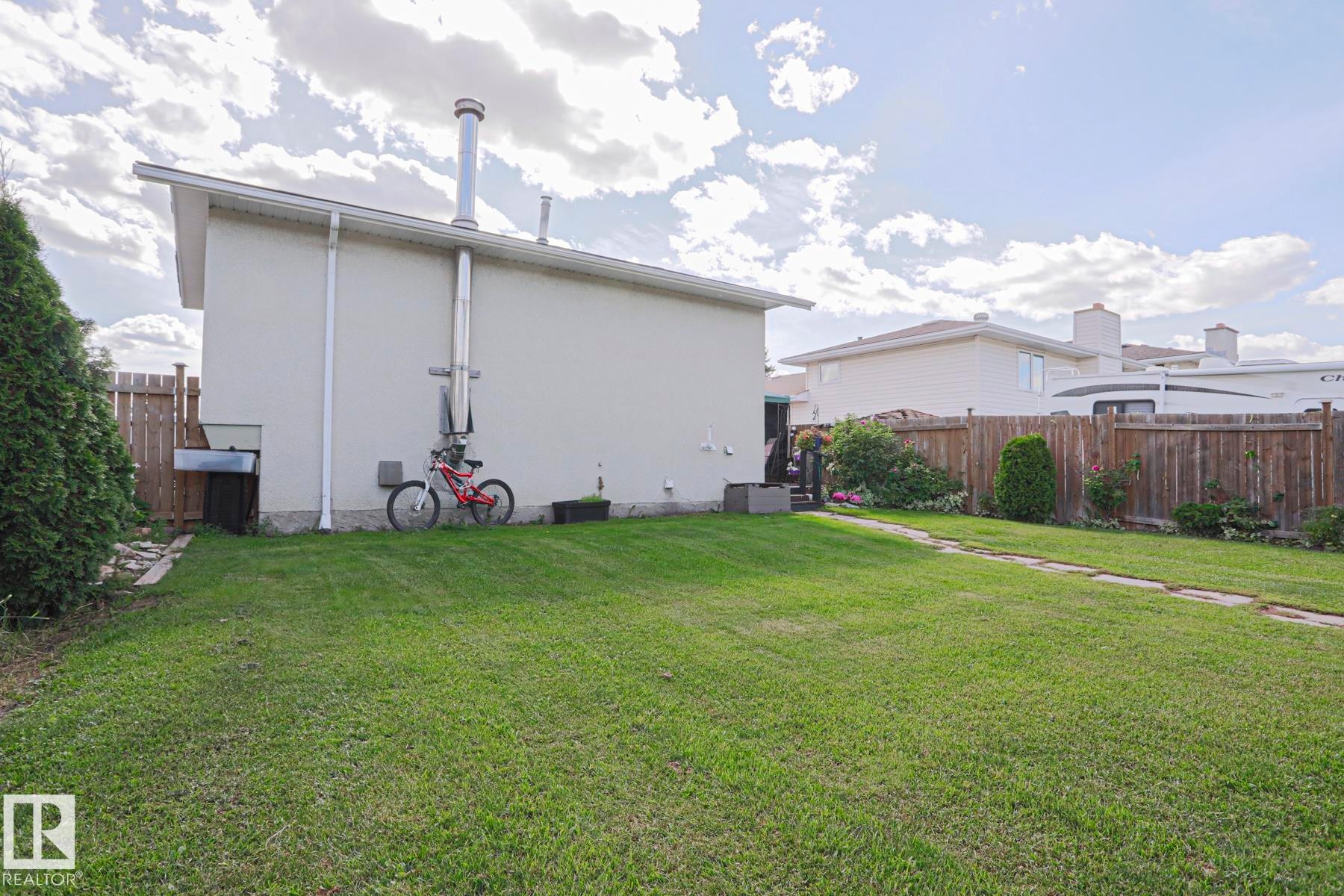Expansive grassy yard with a stone paver pathway, mature perimeter trees, and wood fencing - 11440 144 Avenue Nw, Edmonton, AB