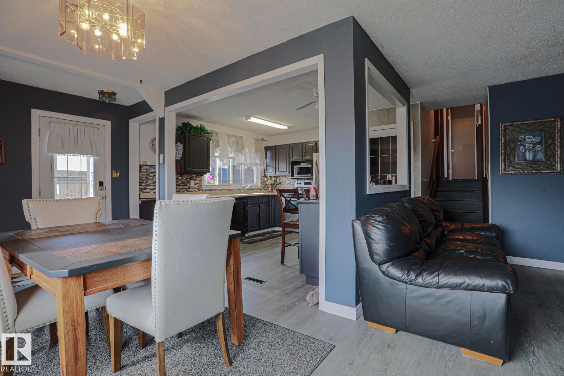 Open-concept living space featuring wood-finish flooring, dark cabinetry, and a modern light fixture - 11440 144 Avenue Nw, Edmonton, AB