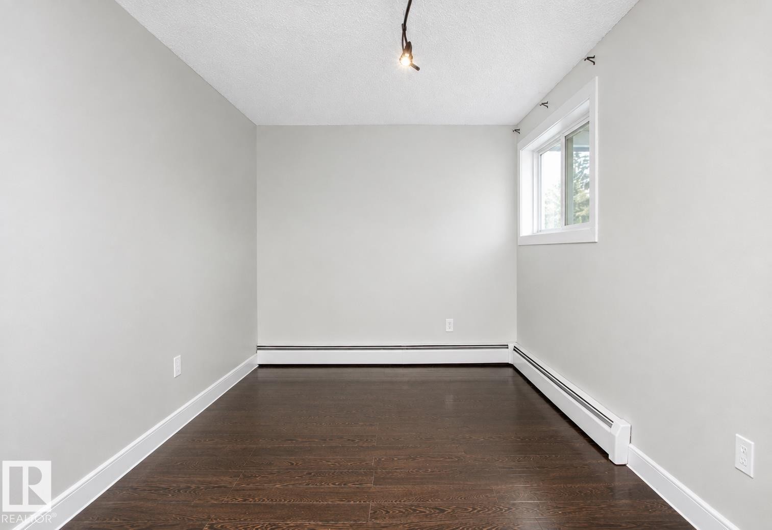 Wood-finish flooring, light gray walls, white trim, track lighting, and a single window - #203 2624 Mill Woods Rd E Nw, Edmonton, AB