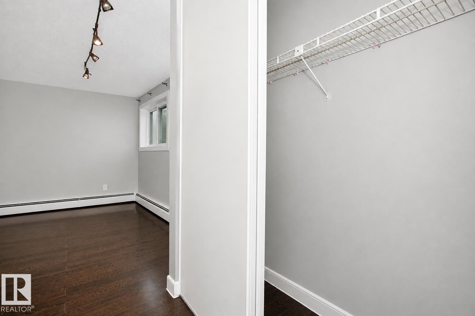 Wood-finish flooring, track lighting, and a window with white trim, complemented by a closet featuring wire shelving - #203 2624 Mill Woods Rd E Nw, Edmonton, AB