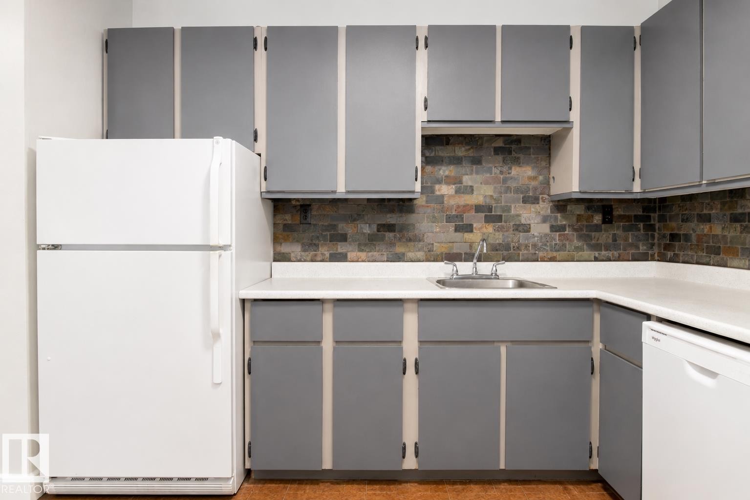Kitchen featuring gray cabinetry, white countertops, stainless steel sink, and brick-style backsplash - #203 2624 Mill Woods Rd E Nw, Edmonton, AB