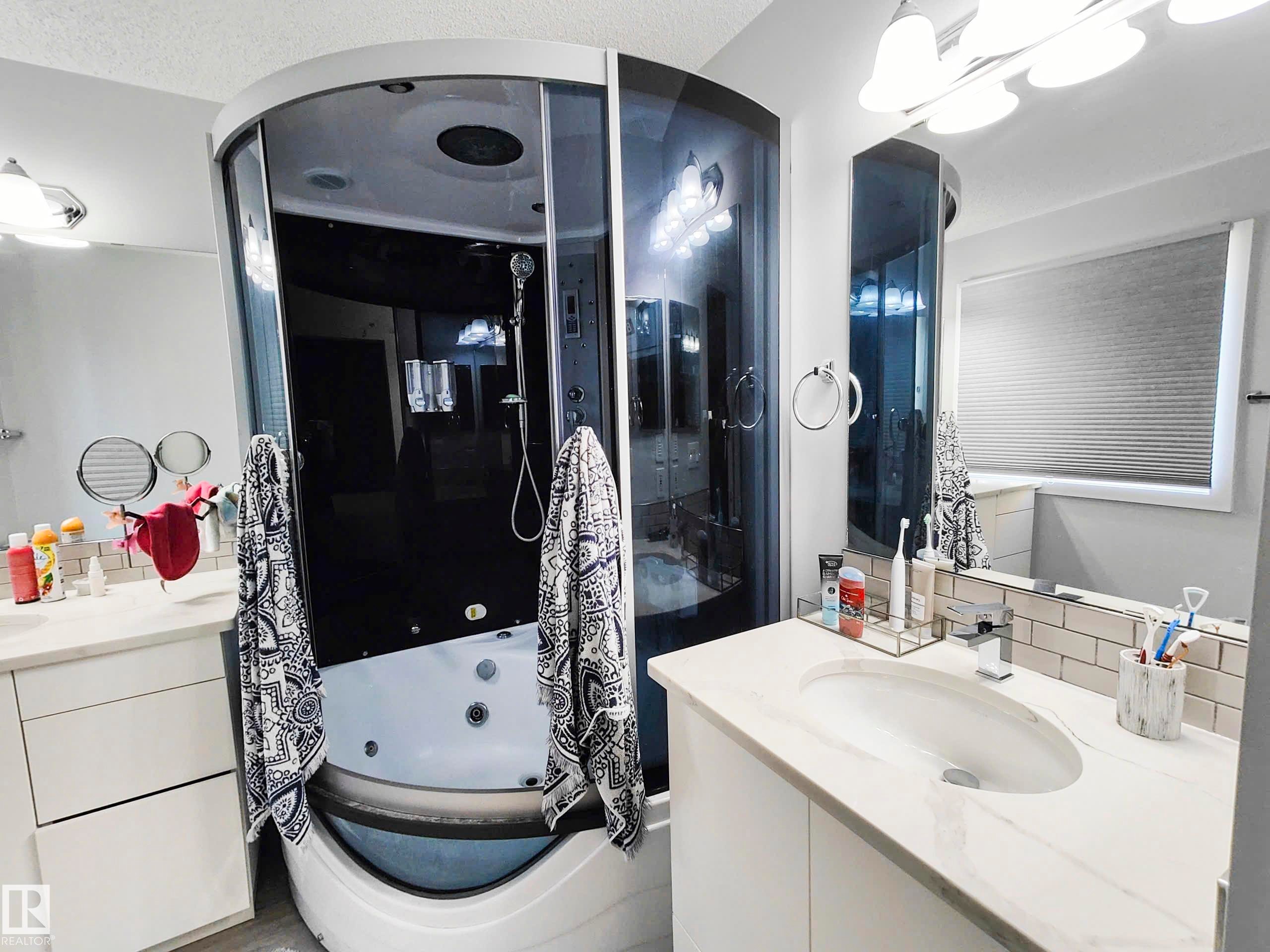 Curved glass shower enclosure with integrated tub, white vanity with an undermount sink, countertop with a polished finish, and a subway tile backsplash - 215 Peter Close Nw, Edmonton, AB