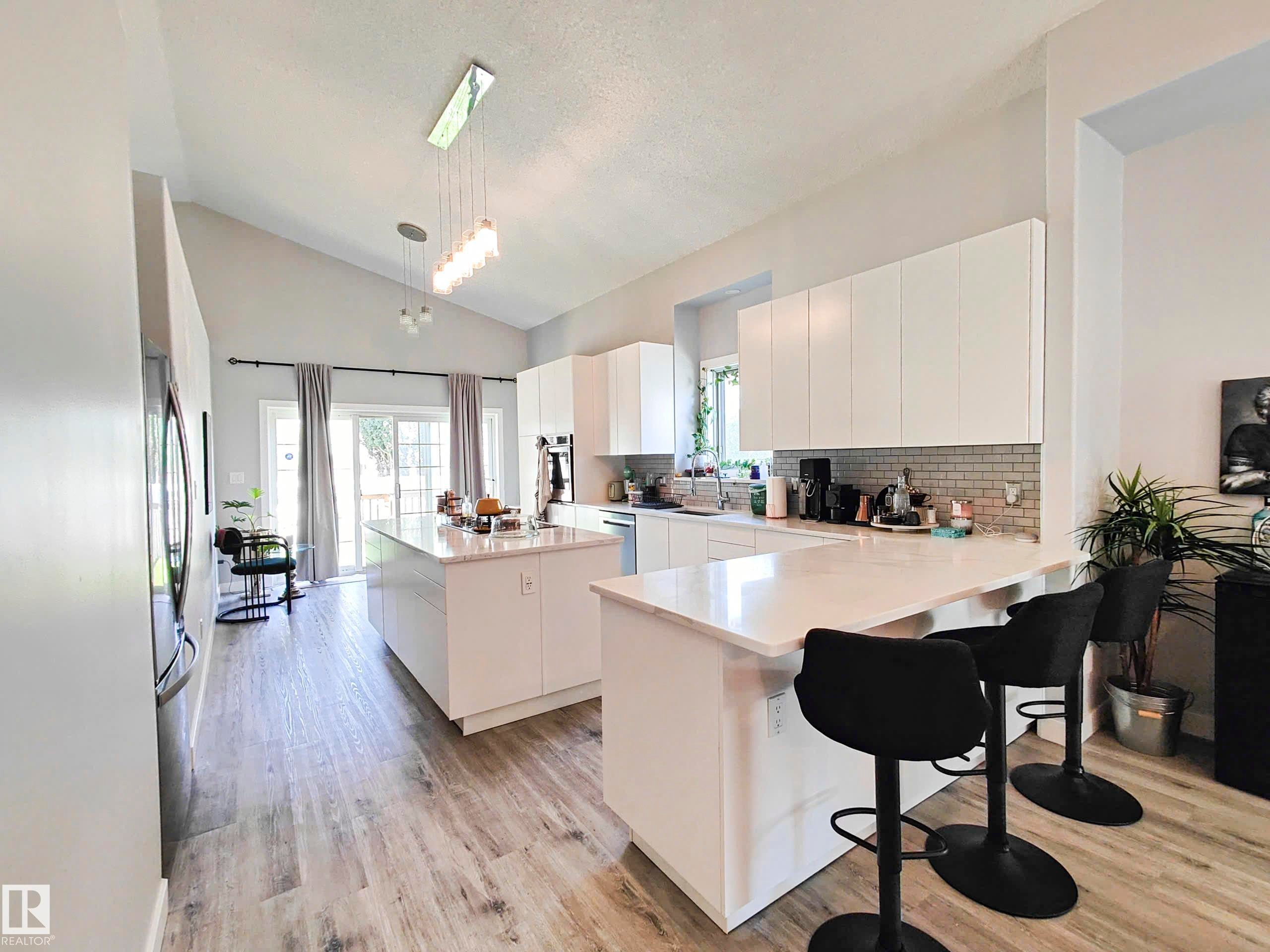 Vaulted ceilings, wood-finish flooring, white flat-panel cabinetry, white solid surface countertops, and a subway tile backsplash - 215 Peter Close Nw, Edmonton, AB
