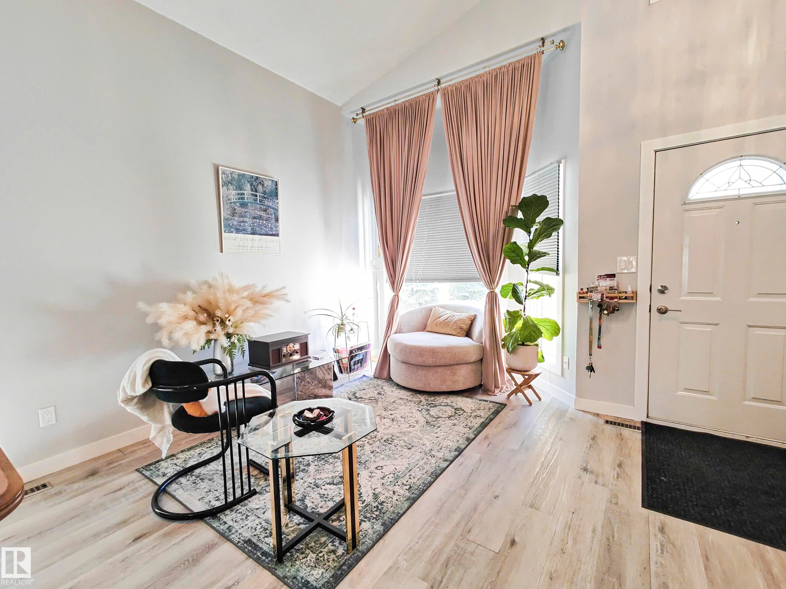 Vaulted ceiling with light-toned walls, wood-finish flooring, and a white entry door with an arched transom window - 215 Peter Close Nw, Edmonton, AB