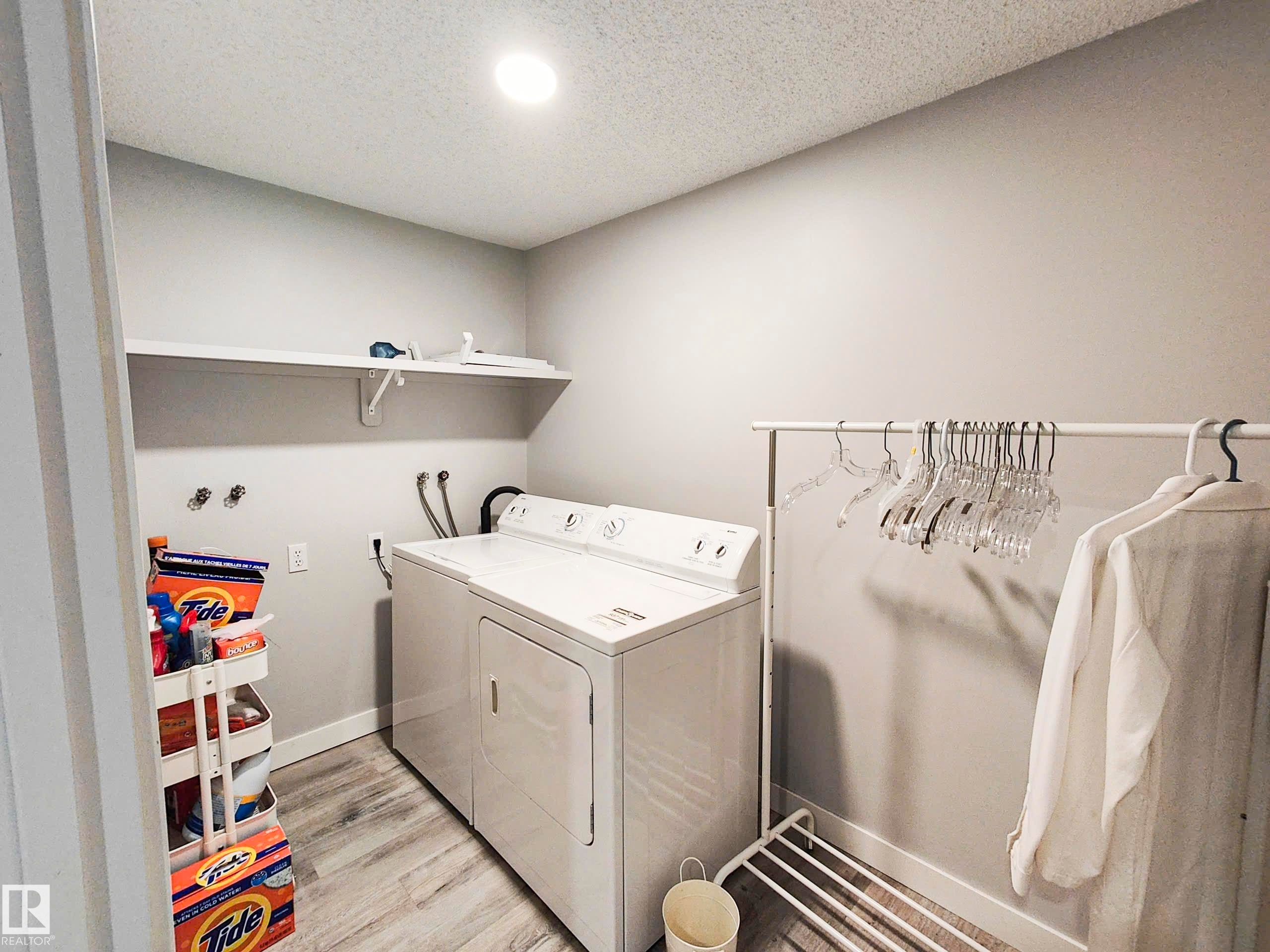 Dedicated laundry area featuring a built-in shelf, overhead lighting, and wood-finish flooring - 215 Peter Close Nw, Edmonton, AB
