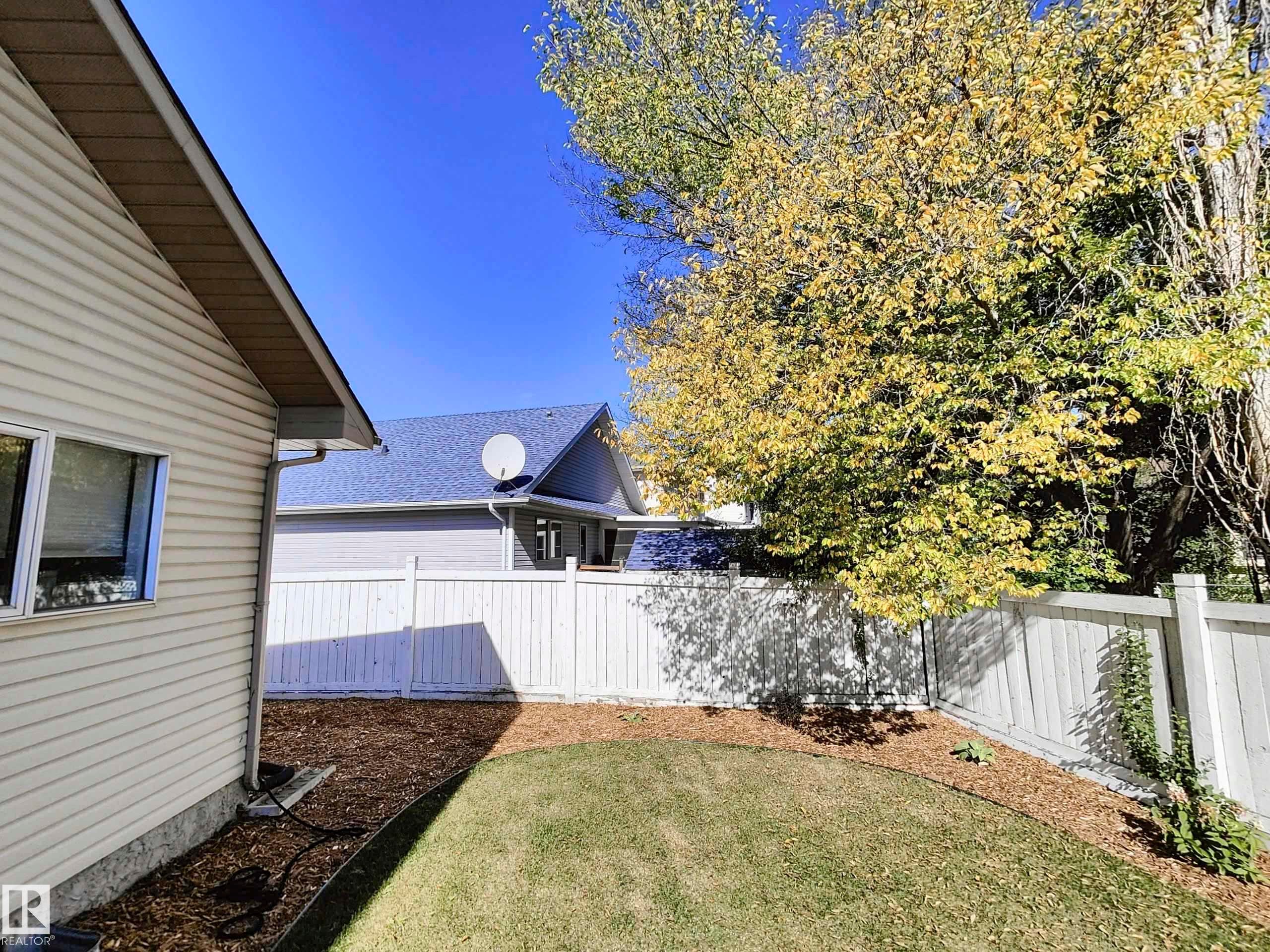 Backyard featuring a privacy fence, manicured lawn, mulched perimeter, and mature trees - 215 Peter Close Nw, Edmonton, AB