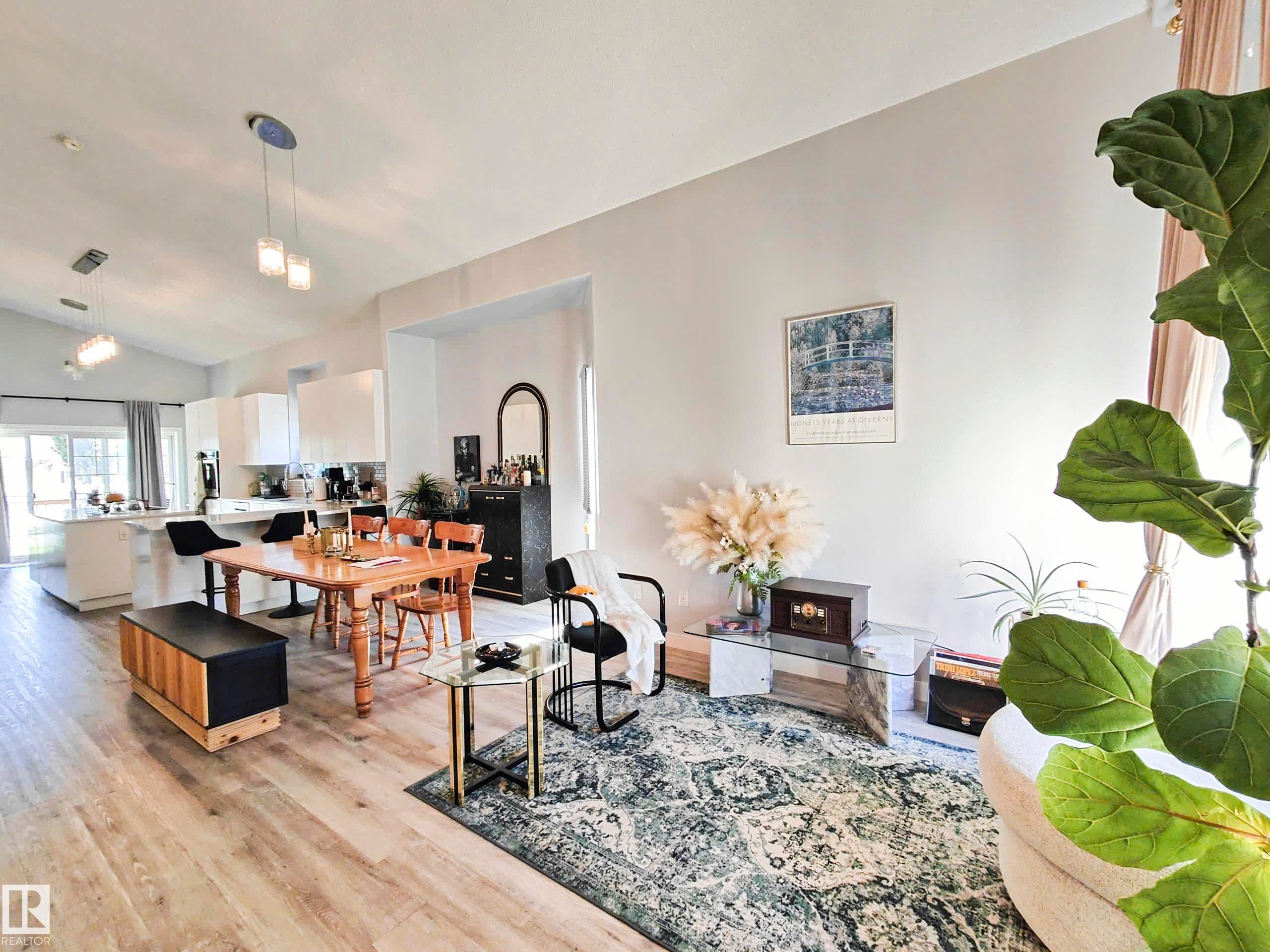 Open-concept living area featuring vaulted ceilings, wood-finish flooring, a kitchen island with seating, and pendant lighting - 215 Peter Close Nw, Edmonton, AB