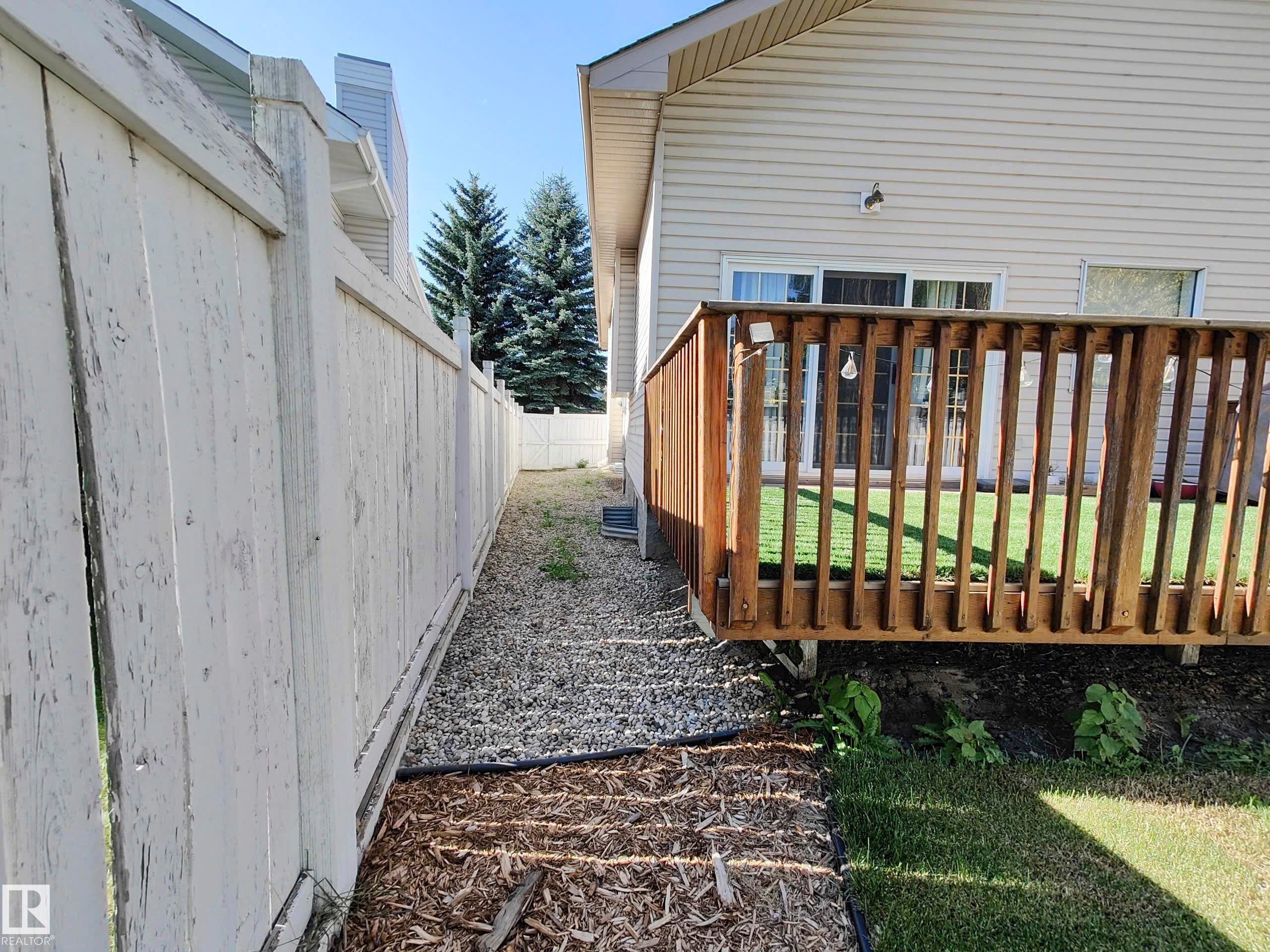 Exterior wood deck with railings, sliding glass door access, and a gravel pathway - 215 Peter Close Nw, Edmonton, AB