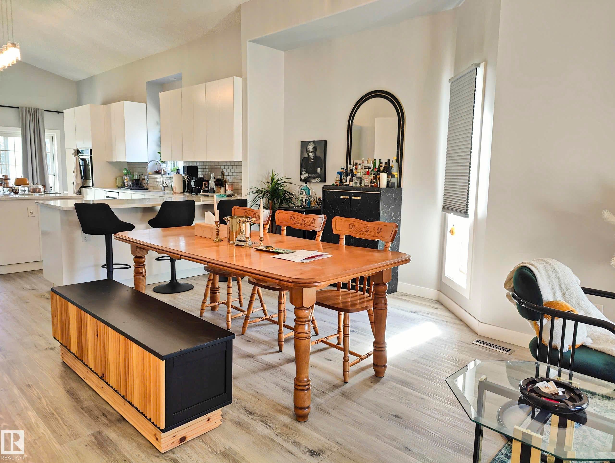 Open-concept living area featuring wood-finish flooring, vaulted ceilings, and a kitchen with white cabinetry and a breakfast bar - 215 Peter Close Nw, Edmonton, AB