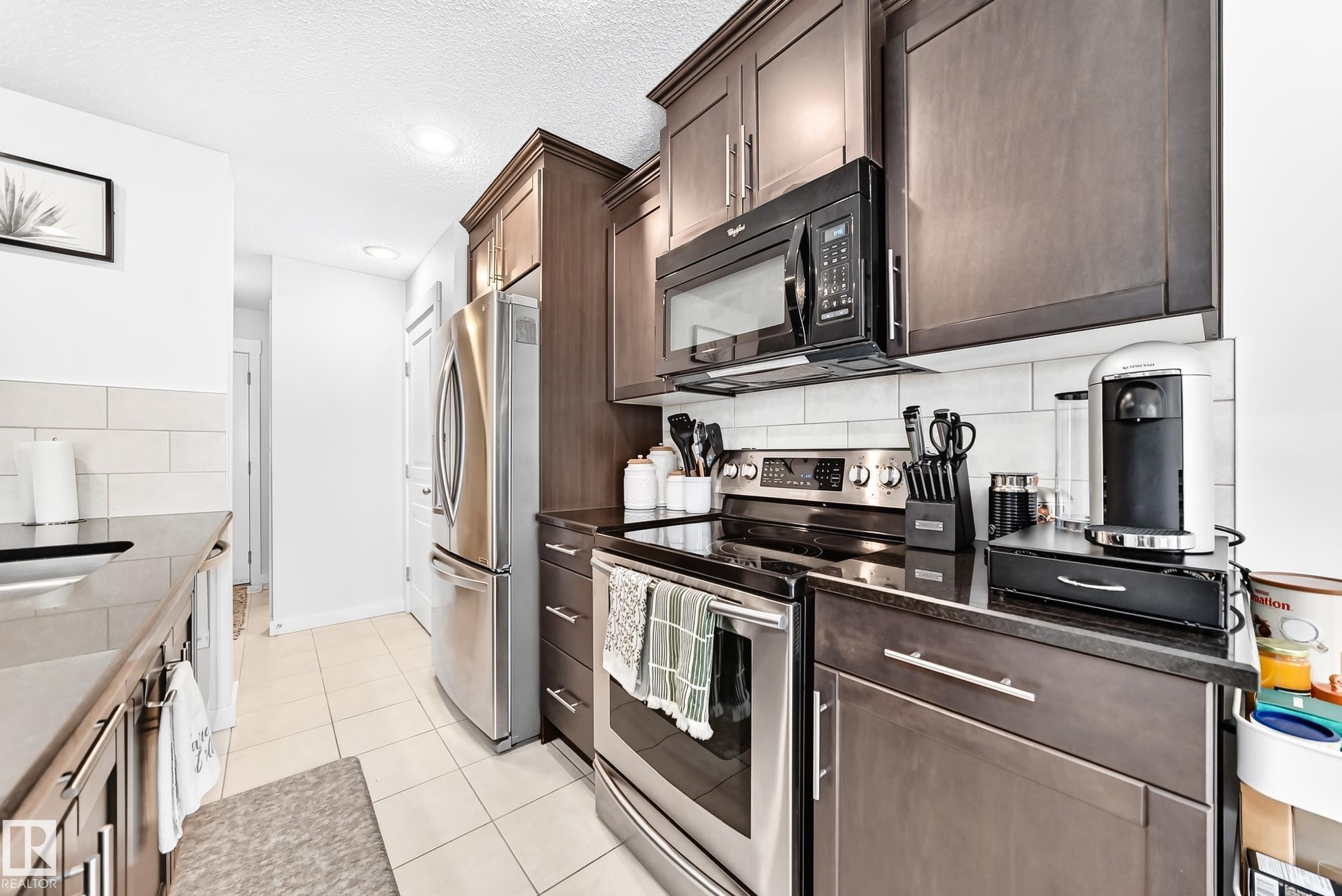 Kitchen featuring dark wood-finish cabinetry, stainless steel appliances, black countertops, a white subway tile backsplash, and recessed lighting - 16832 53 Street Nw, Edmonton, AB
