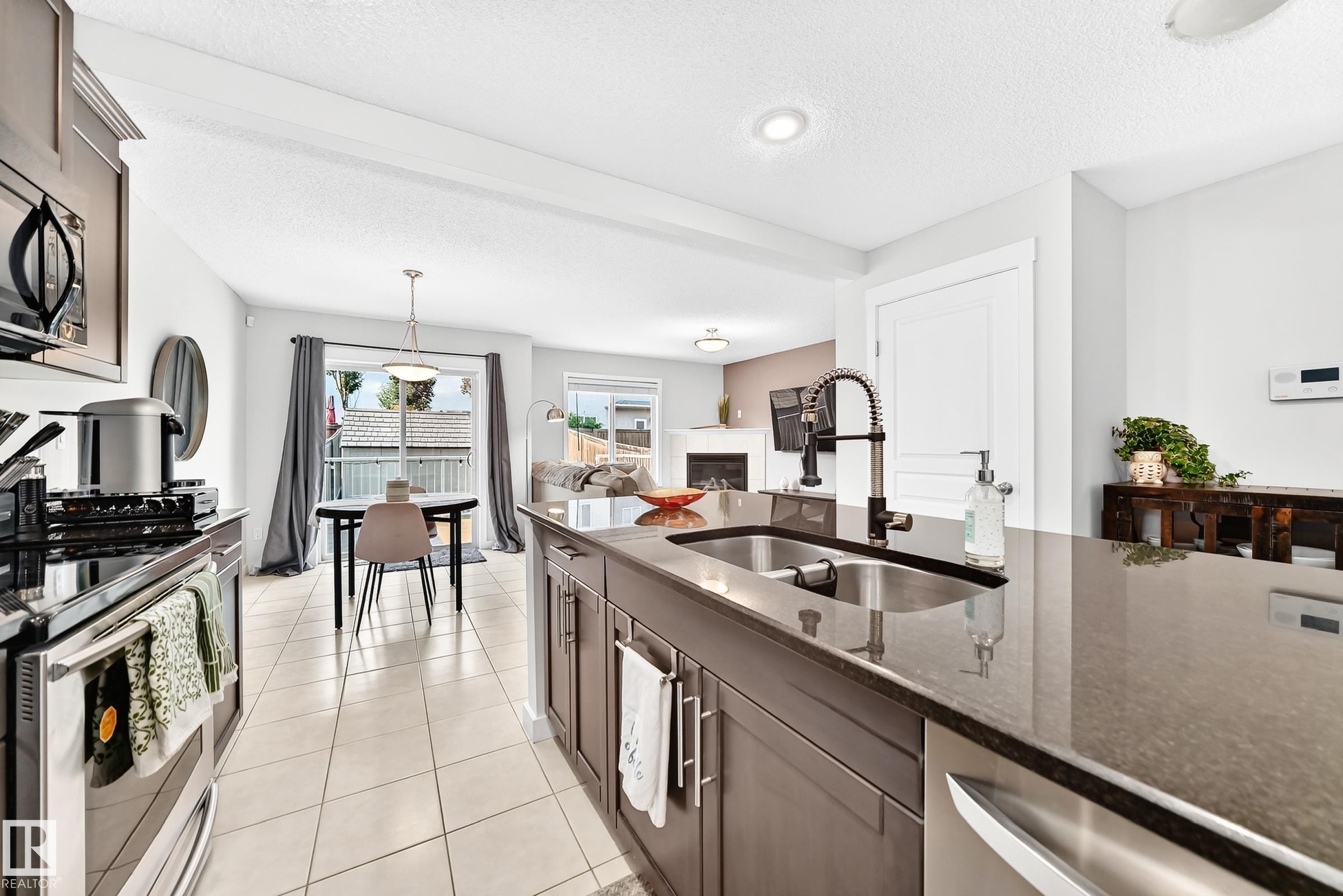 Open-concept kitchen with a large island, stainless steel appliances, dark cabinetry, and a double basin sink with a gooseneck faucet - 16832 53 Street Nw, Edmonton, AB