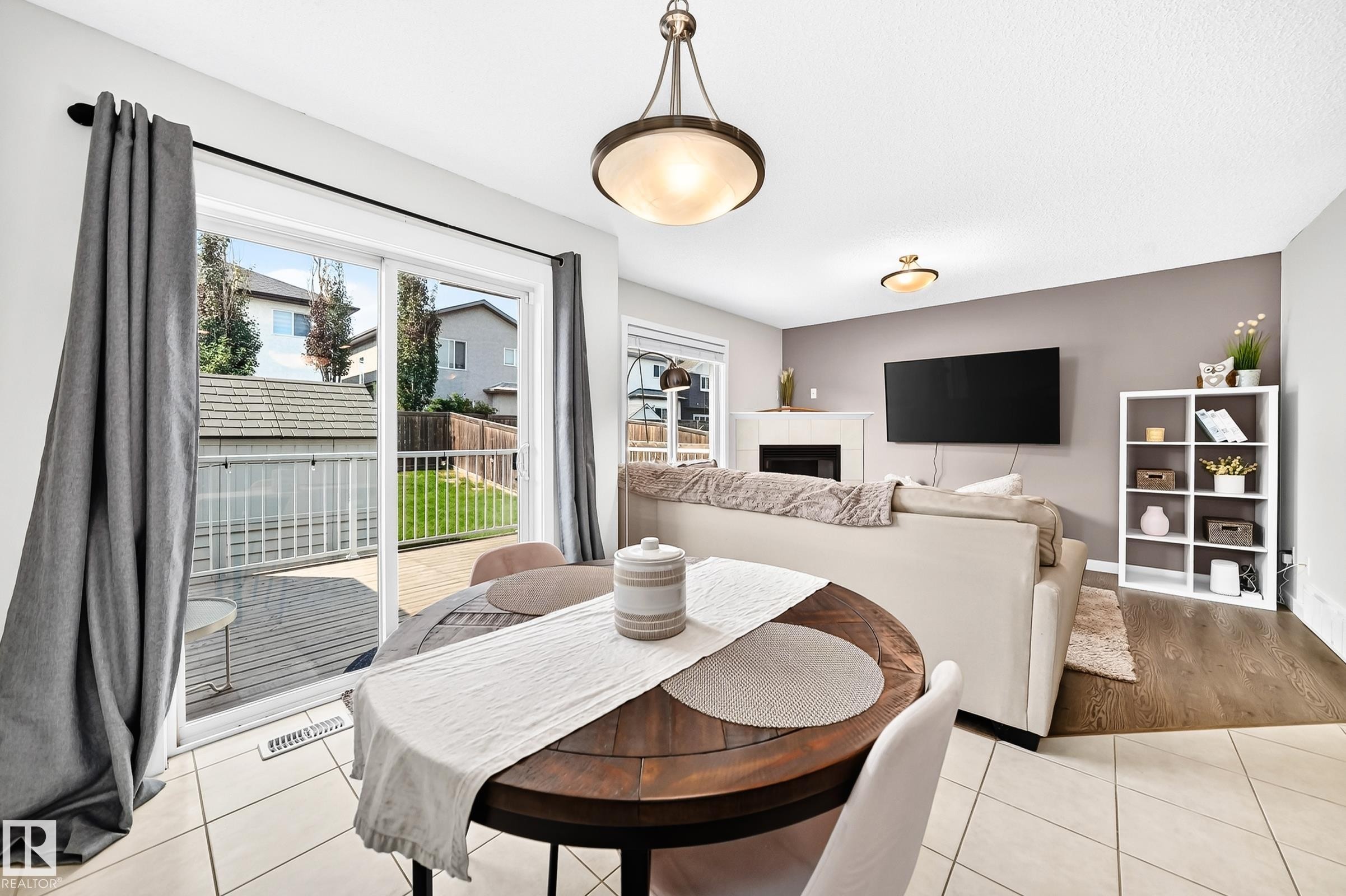 Open-concept living area with a fireplace, hard-surface flooring, and a sliding glass door leading to an outdoor deck and fenced yard - 16832 53 Street Nw, Edmonton, AB