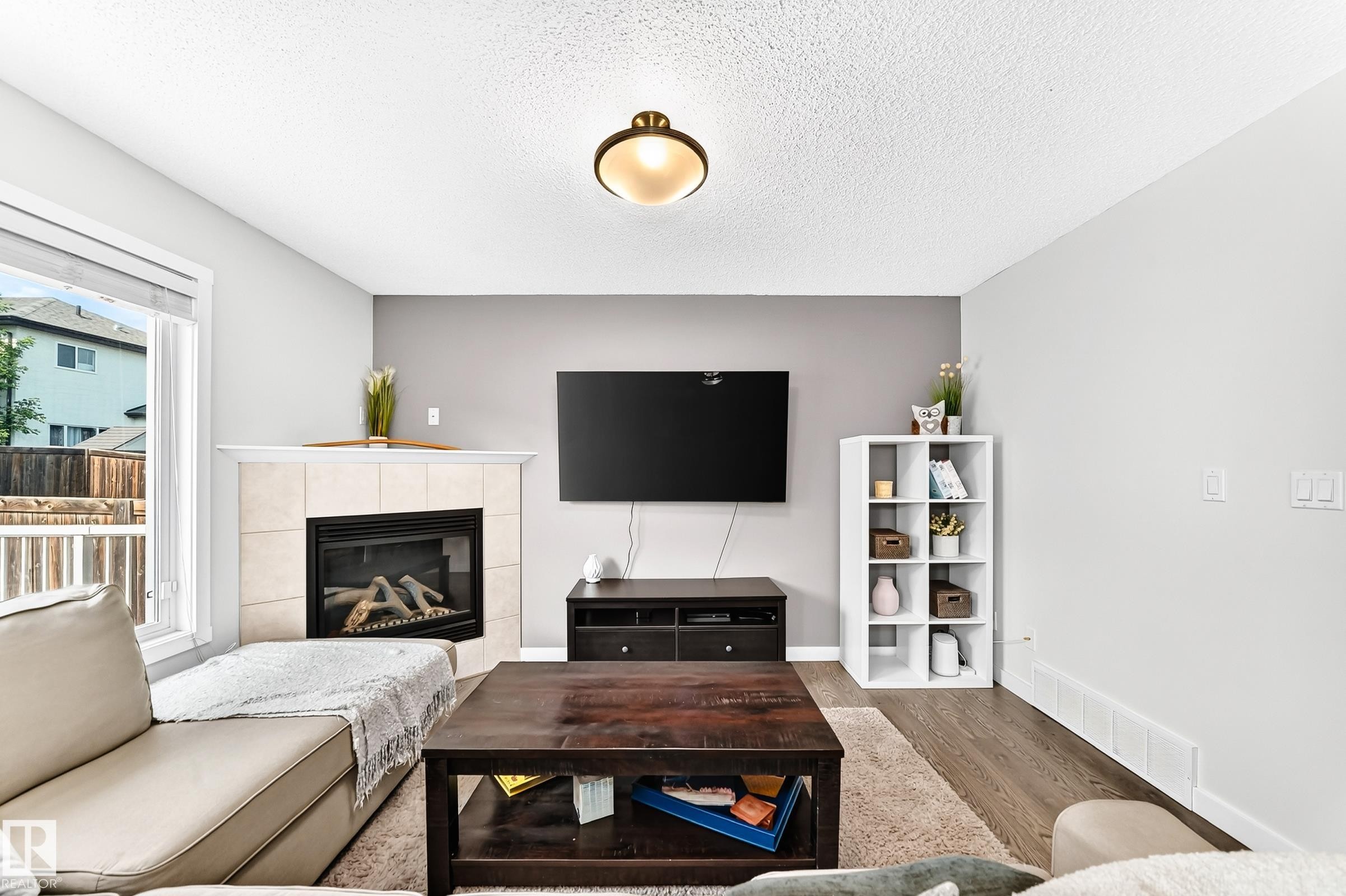 Corner fireplace with tile surround, wood-finish flooring, and recessed ceiling light fixture - 16832 53 Street Nw, Edmonton, AB