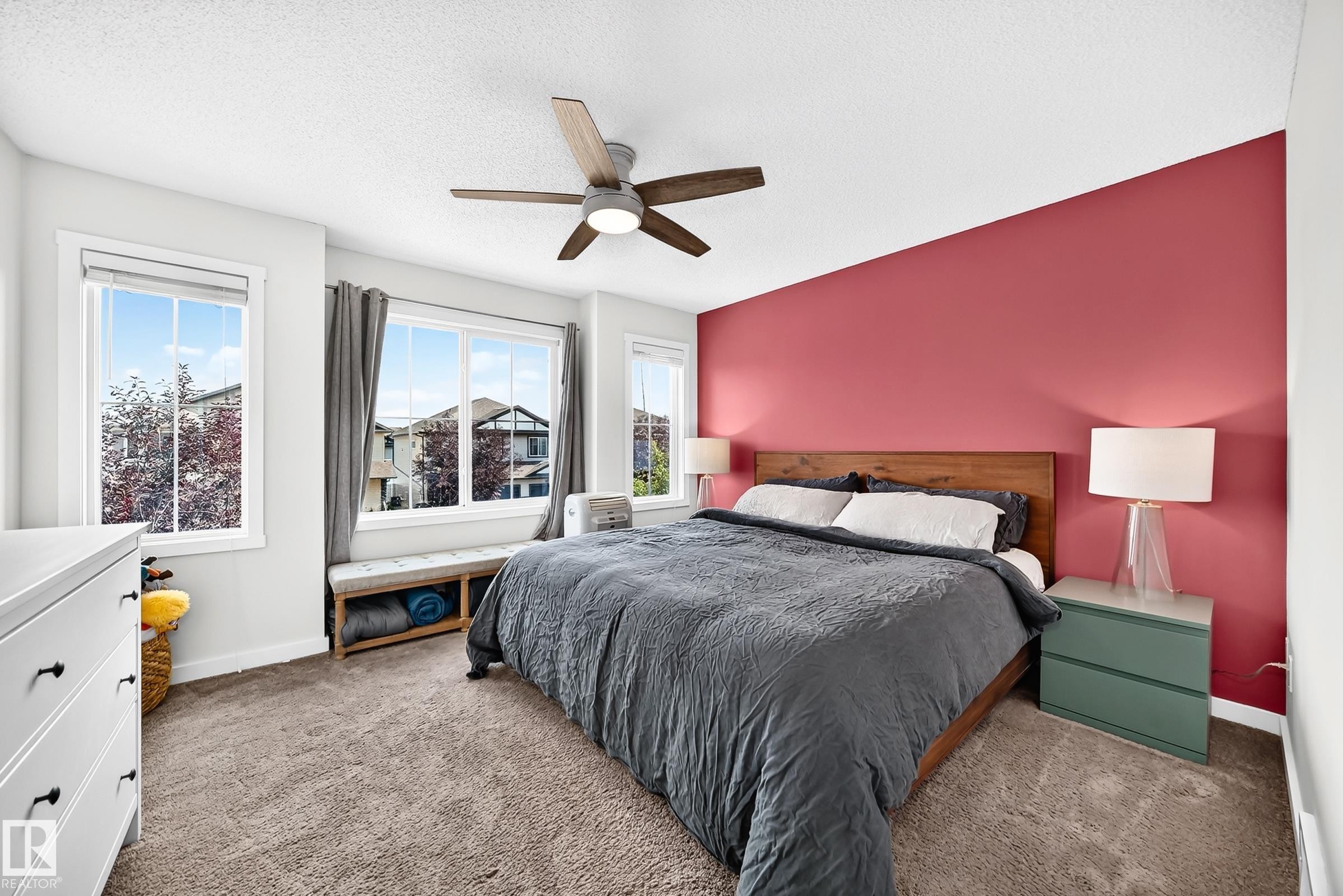 Carpeted room with multiple windows, a ceiling fan with integrated lighting, and a wood-finish headboard - 16832 53 Street Nw, Edmonton, AB
