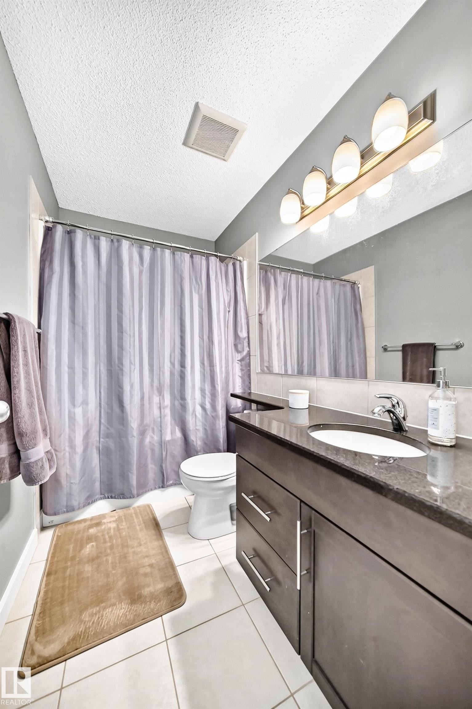 White tile flooring with a dark wood-finish vanity, integrated sink, and a large mirror - 16832 53 Street Nw, Edmonton, AB