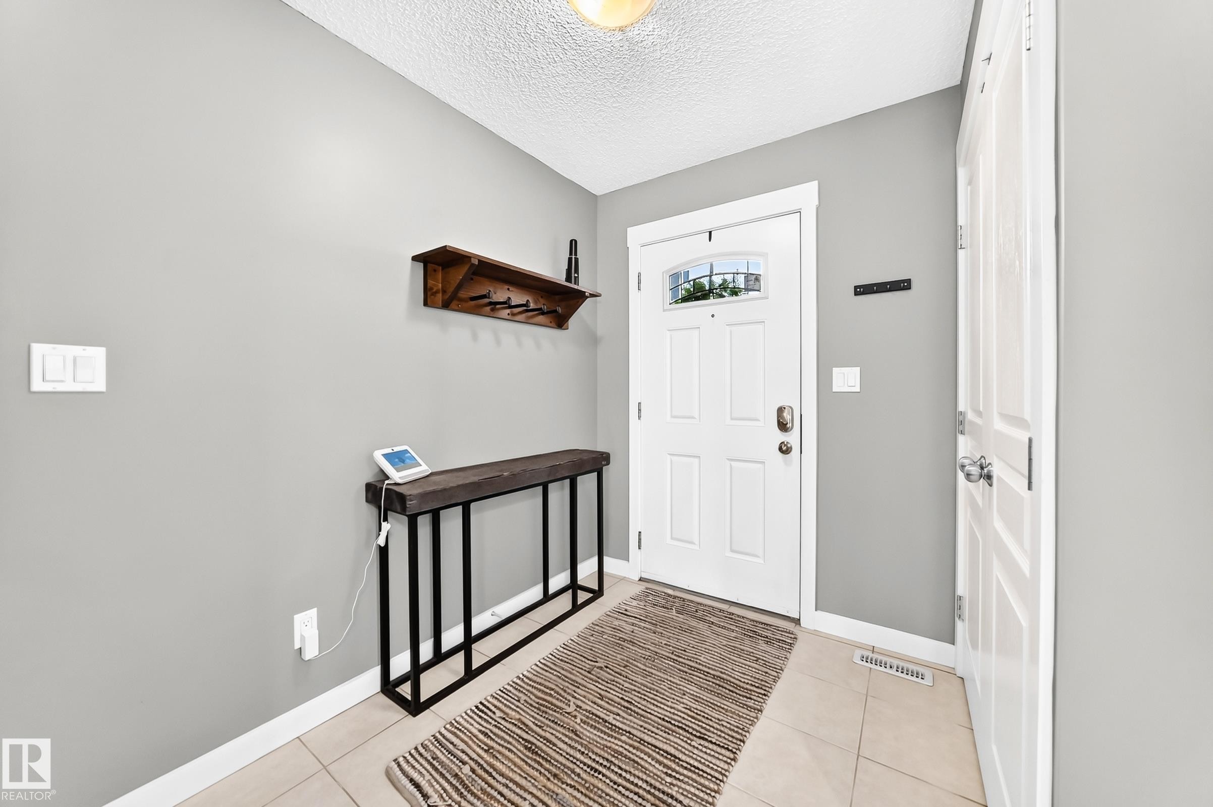 Tiled flooring entryway featuring a white paneled door with windowpane detailing and a white paneled closet door - 16832 53 Street Nw, Edmonton, AB