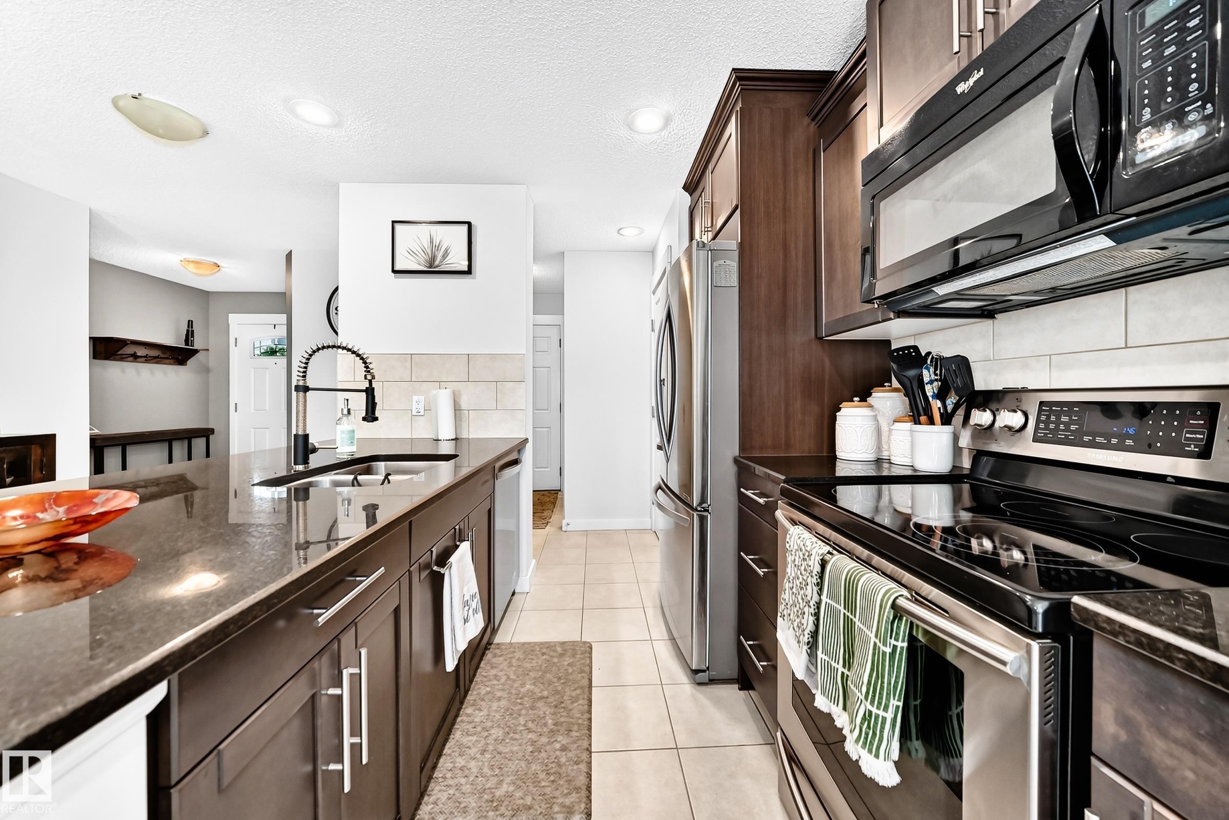 Kitchen featuring dark wood-finish cabinetry, stainless steel appliances, a black electric range, a black microwave, and tile flooring - 16832 53 Street Nw, Edmonton, AB