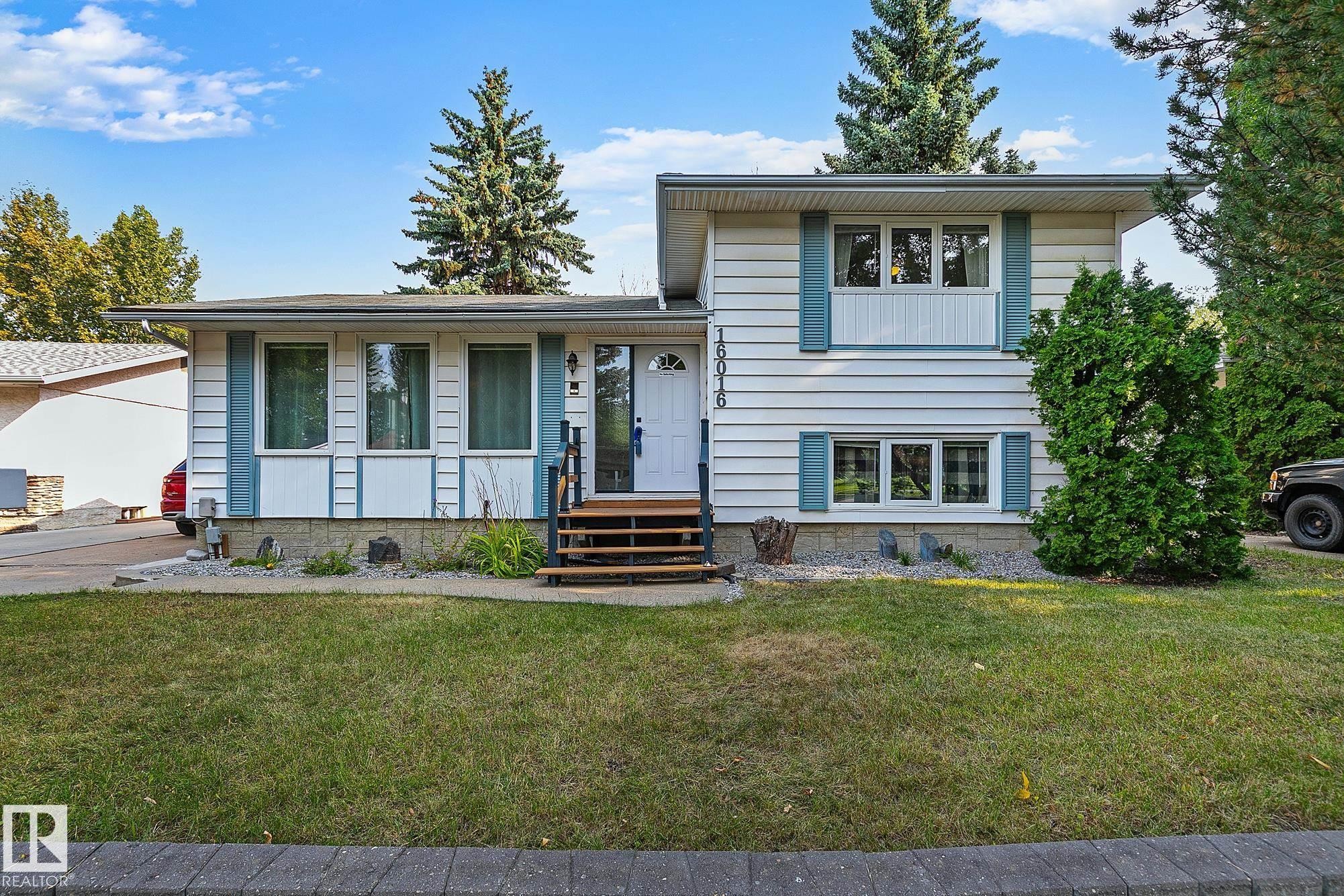 White siding exterior with blue decorative shutters, a wooden entry staircase, and a manicured front lawn - 16016 78A Avenue Nw, Edmonton, AB