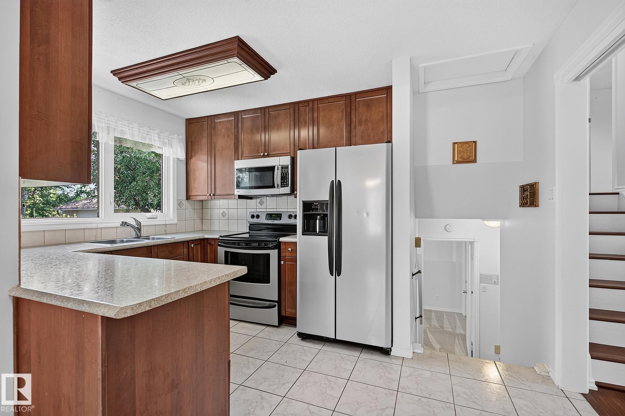 Kitchen featuring wood-finish cabinetry, stainless steel appliances, and a tiled backsplash - 16016 78A Avenue Nw, Edmonton, AB