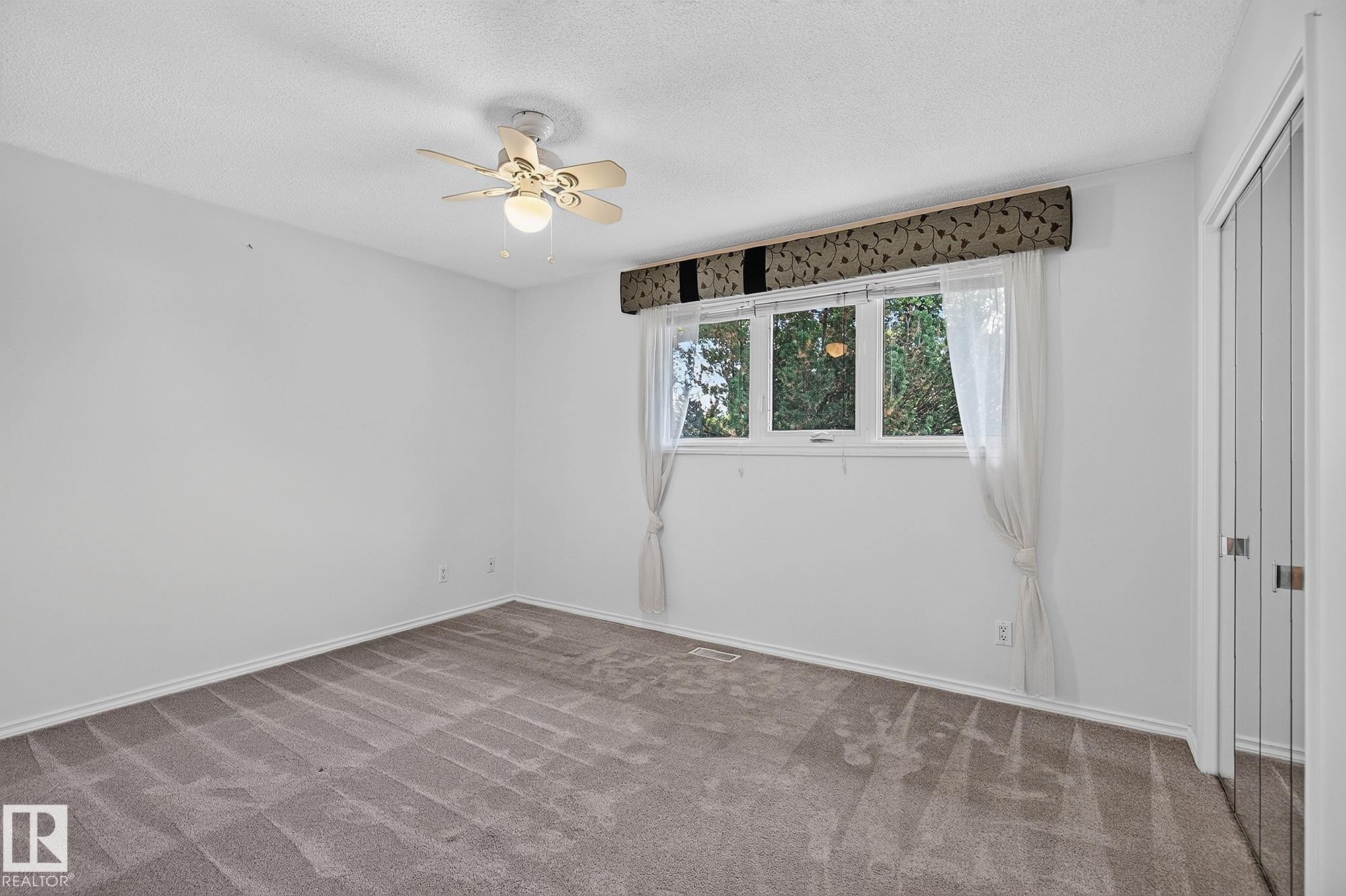 Neutral carpeted flooring, white walls, ceiling fan with integrated lighting, window with a patterned valance, and bi-fold closet doors - 16016 78A Avenue Nw, Edmonton, AB