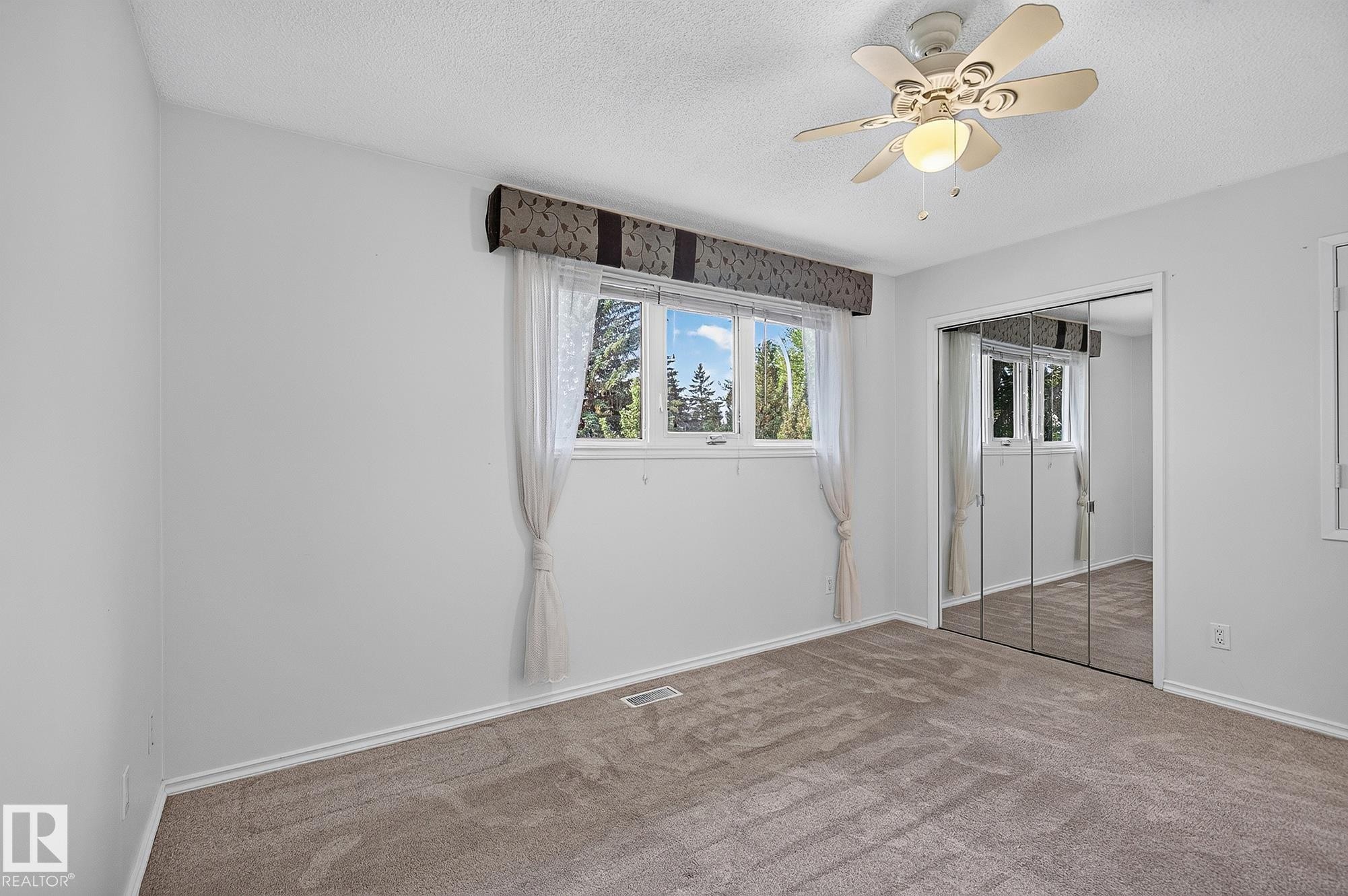 Ceiling fan with integrated lighting, window with exterior scenery, mirrored closet doors, and neutral carpeting - 16016 78A Avenue Nw, Edmonton, AB