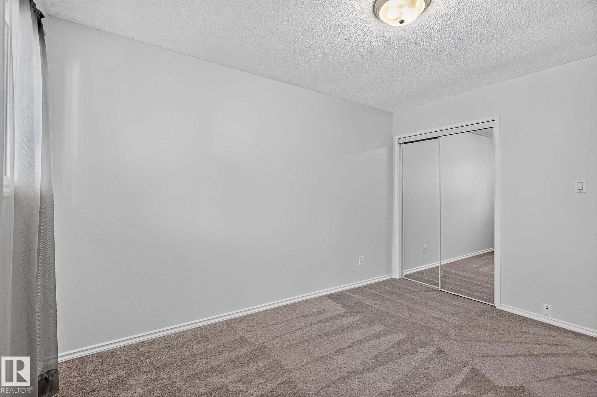 Wall-to-wall carpeting with a geometric pattern, mirrored closet doors, and flush-mount ceiling lighting - 16016 78A Avenue Nw, Edmonton, AB