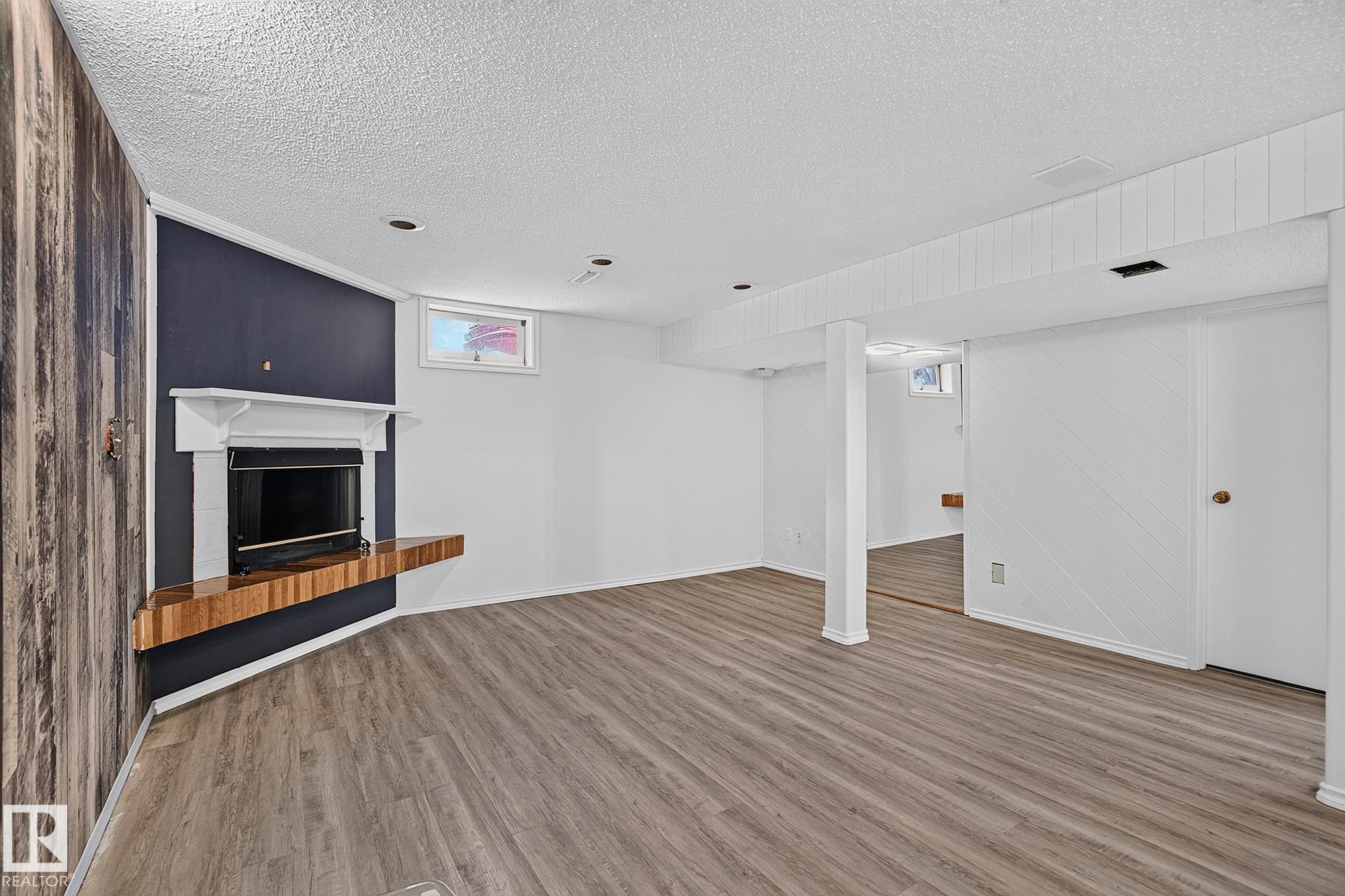 Spacious room featuring wood-finish flooring, a built-in fireplace with a mantel, and recessed lighting - 16016 78A Avenue Nw, Edmonton, AB