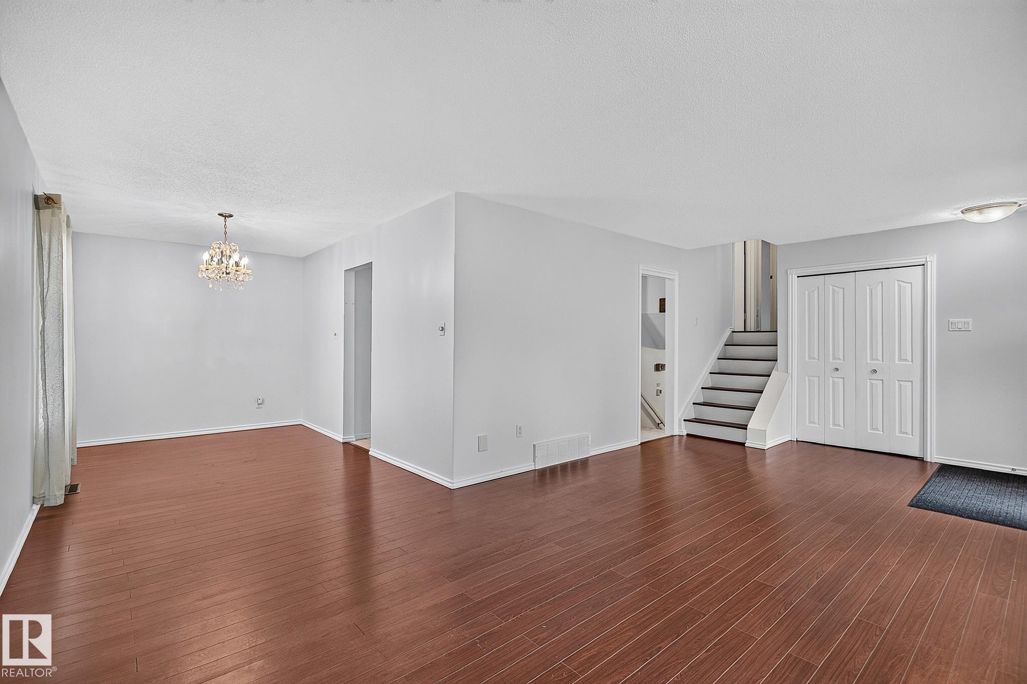 Spacious room featuring wood-finish flooring, a crystal chandelier, and neutral wall tones - 16016 78A Avenue Nw, Edmonton, AB