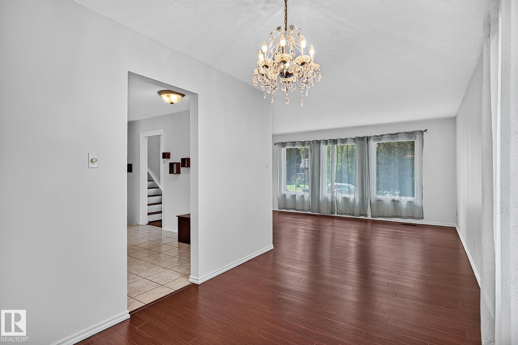 Hardwood flooring, crystal chandelier, neutral wall paint, three large windows, and an arched entryway - 16016 78A Avenue Nw, Edmonton, AB