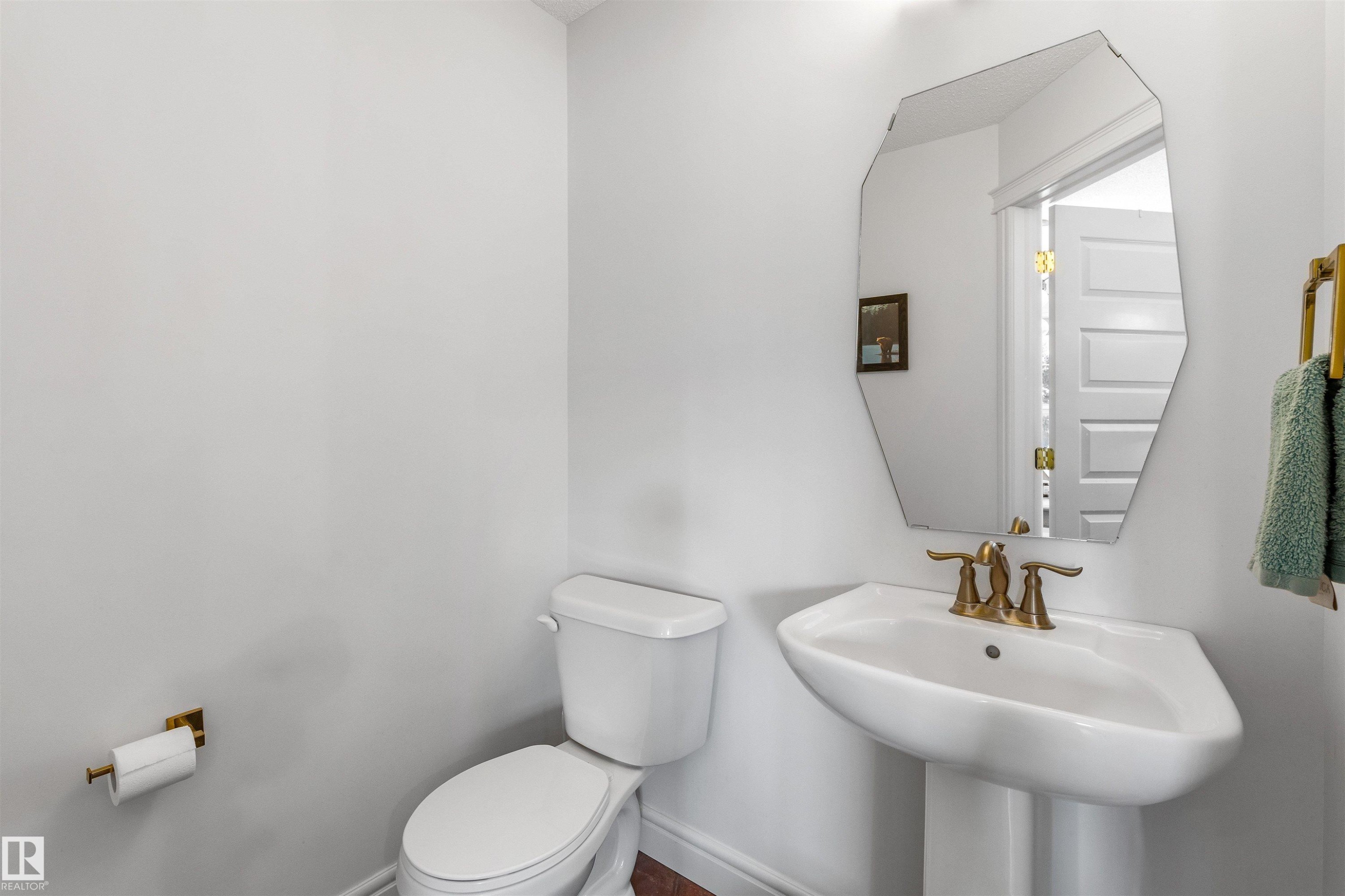 Pedestal sink with brass-finish faucet, geometric wall mirror, and white toilet - #71 330 Bulyea Rd Nw, Edmonton, AB