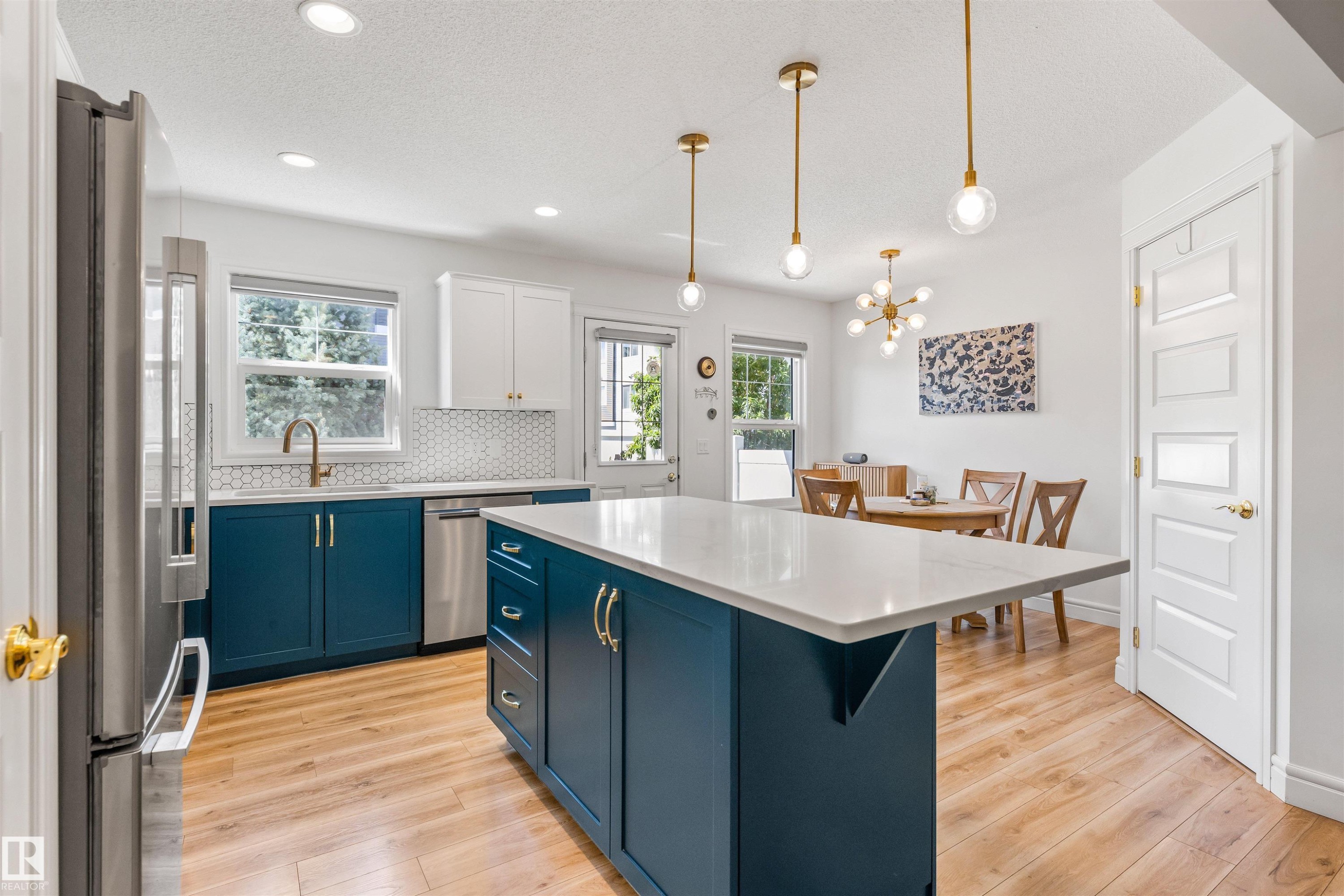 Kitchen featuring two-tone cabinetry, wood-finish flooring, a central island with countertop, and stainless steel appliances - #71 330 Bulyea Rd Nw, Edmonton, AB