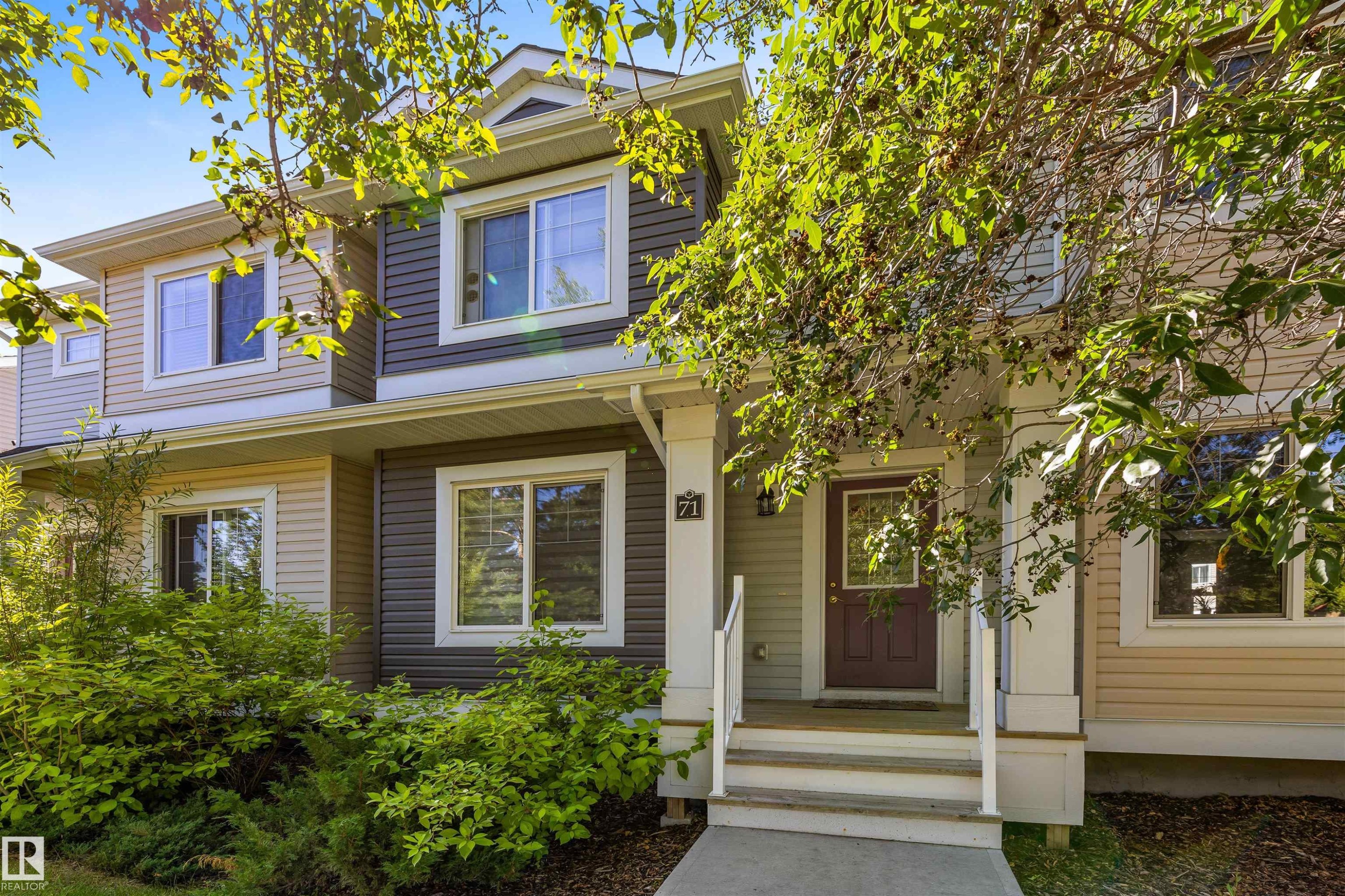 Two-story exterior with multi-toned siding, white trim windows, covered porch, and mature front landscaping - #71 330 Bulyea Rd Nw, Edmonton, AB
