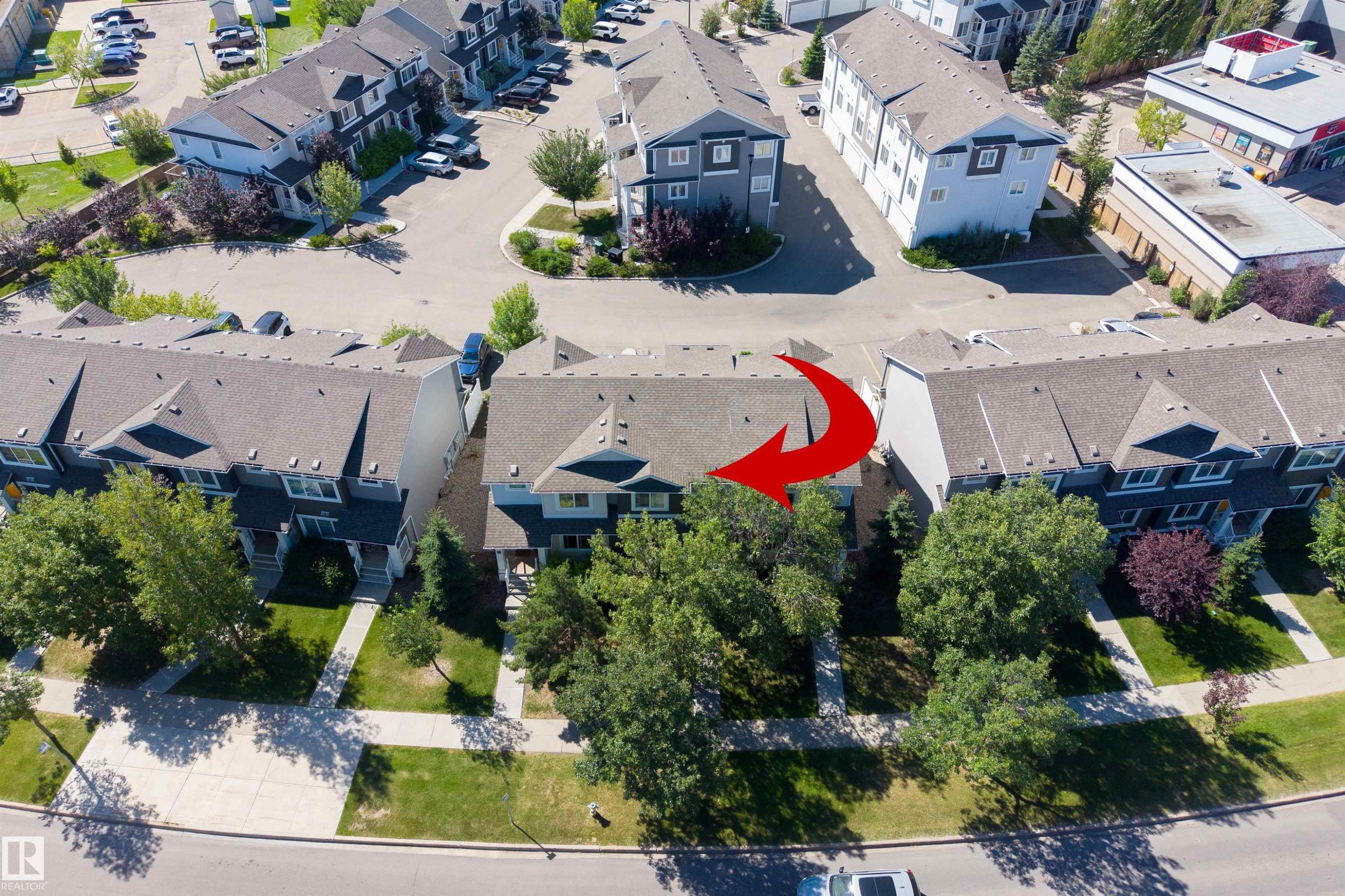 Townhome with a gray pitched roof, mature trees, green lawn, and concrete walkways - #71 330 Bulyea Rd Nw, Edmonton, AB