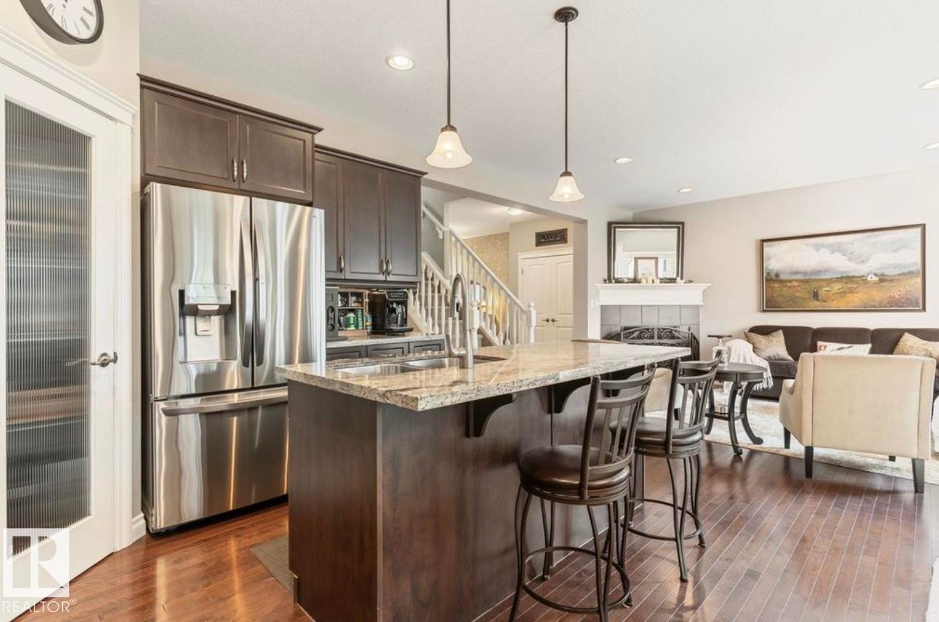 Kitchen with granite island, stainless steel refrigerator, dark wood cabinetry, and wood-finish flooring - 22 Voleta Crest, Spruce Grove, AB